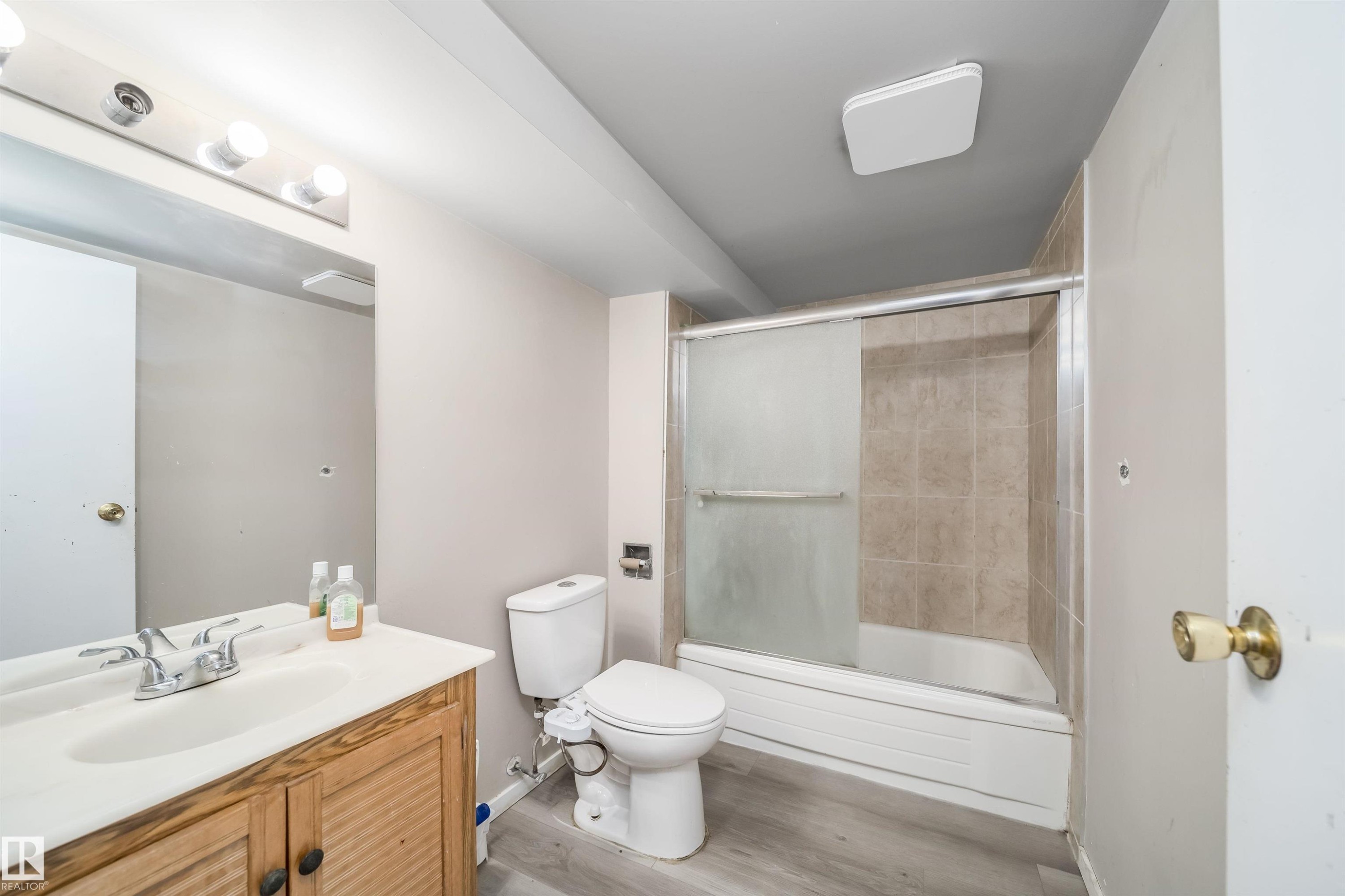 Bathroom featuring a vanity with a white countertop and wood-finish cabinetry, a toilet, and a tub with a sliding glass enclosure and tiled surround - 1771 37 Street, Edmonton, AB - Indoor Photo Showing Bathroom