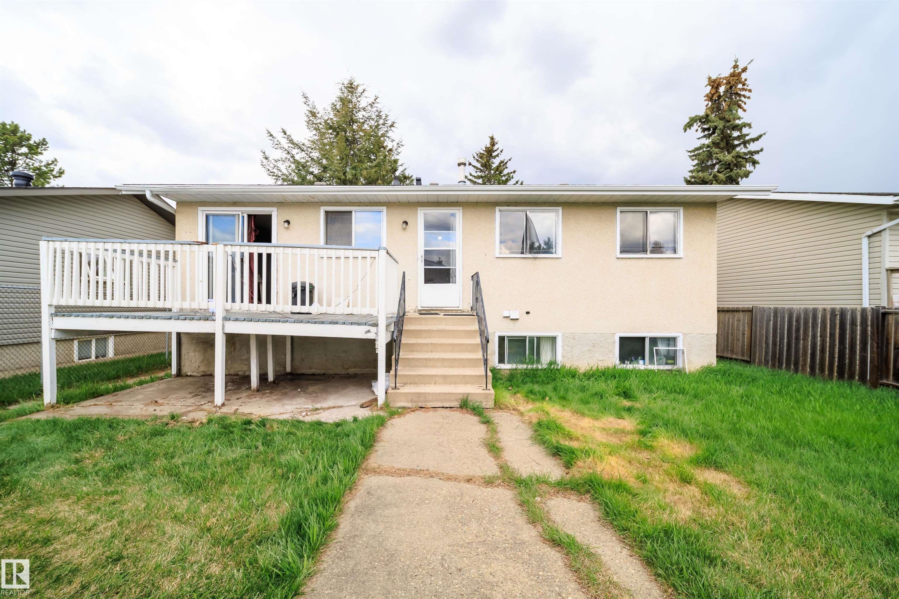 Rear exterior featuring a raised white deck with balustrade, ground-level concrete patio, and a concrete pathway - 1771 37 Street, Edmonton, AB - Outdoor With Deck Patio Veranda