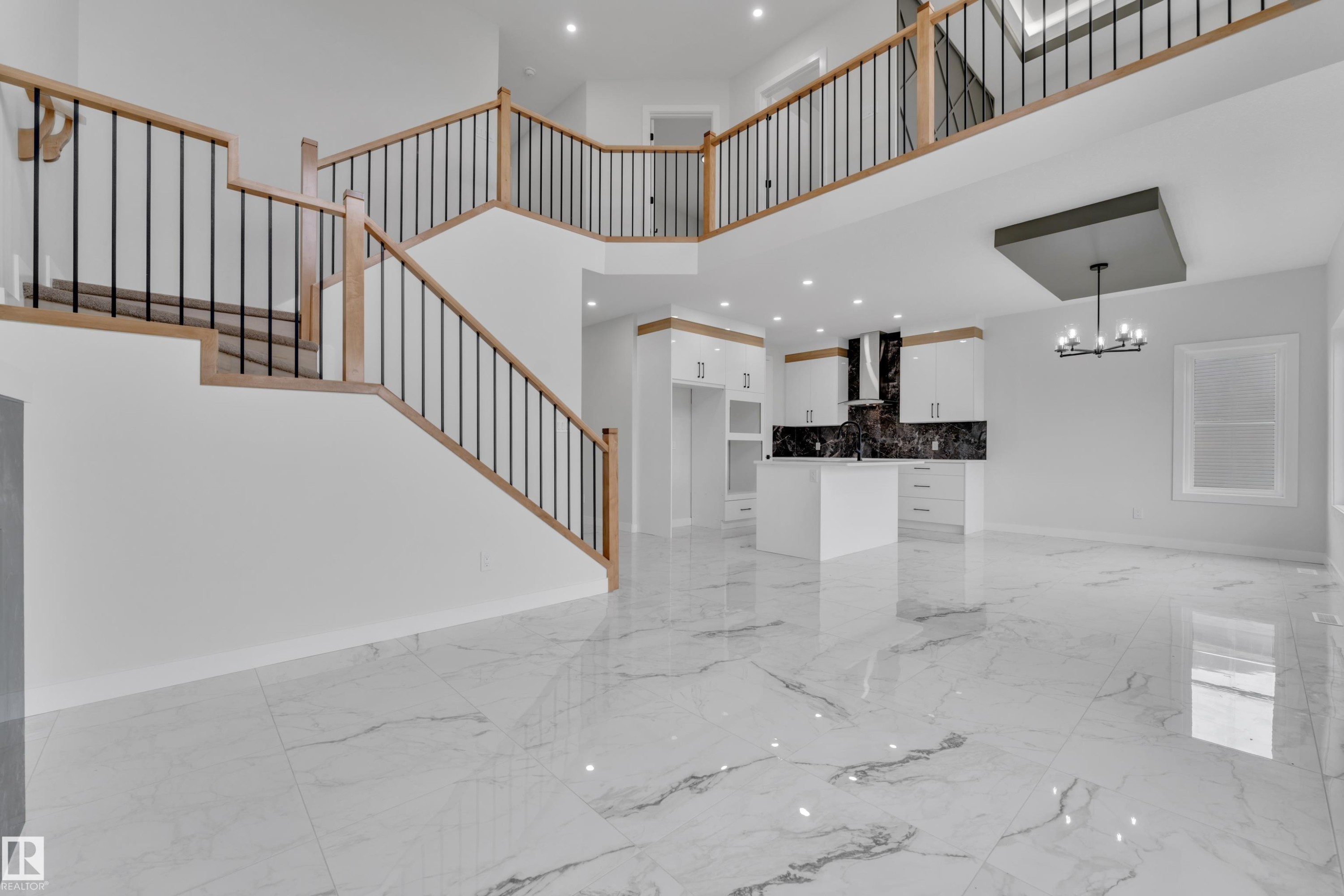 Open-concept interior featuring a grand staircase with wood railings and black spindles, large format marble-look tile flooring, and a modern kitchen with white cabinetry and dark stone backsplash - 12623 44 Street, Edmonton, AB