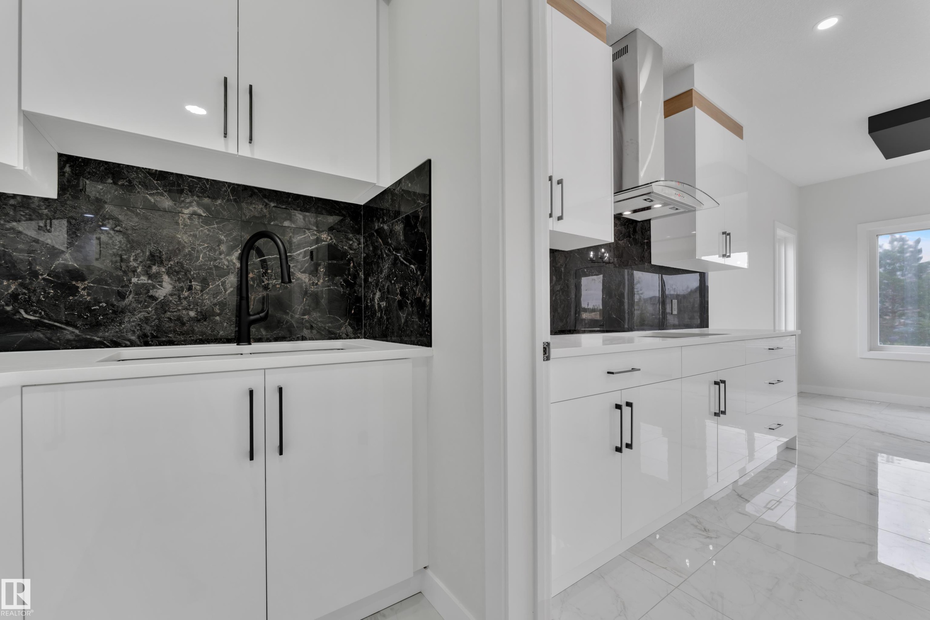 Modern kitchen featuring a sleek black backsplash, white cabinetry with contemporary hardware, and a stainless steel range hood - 12623 44 Street, Edmonton, AB