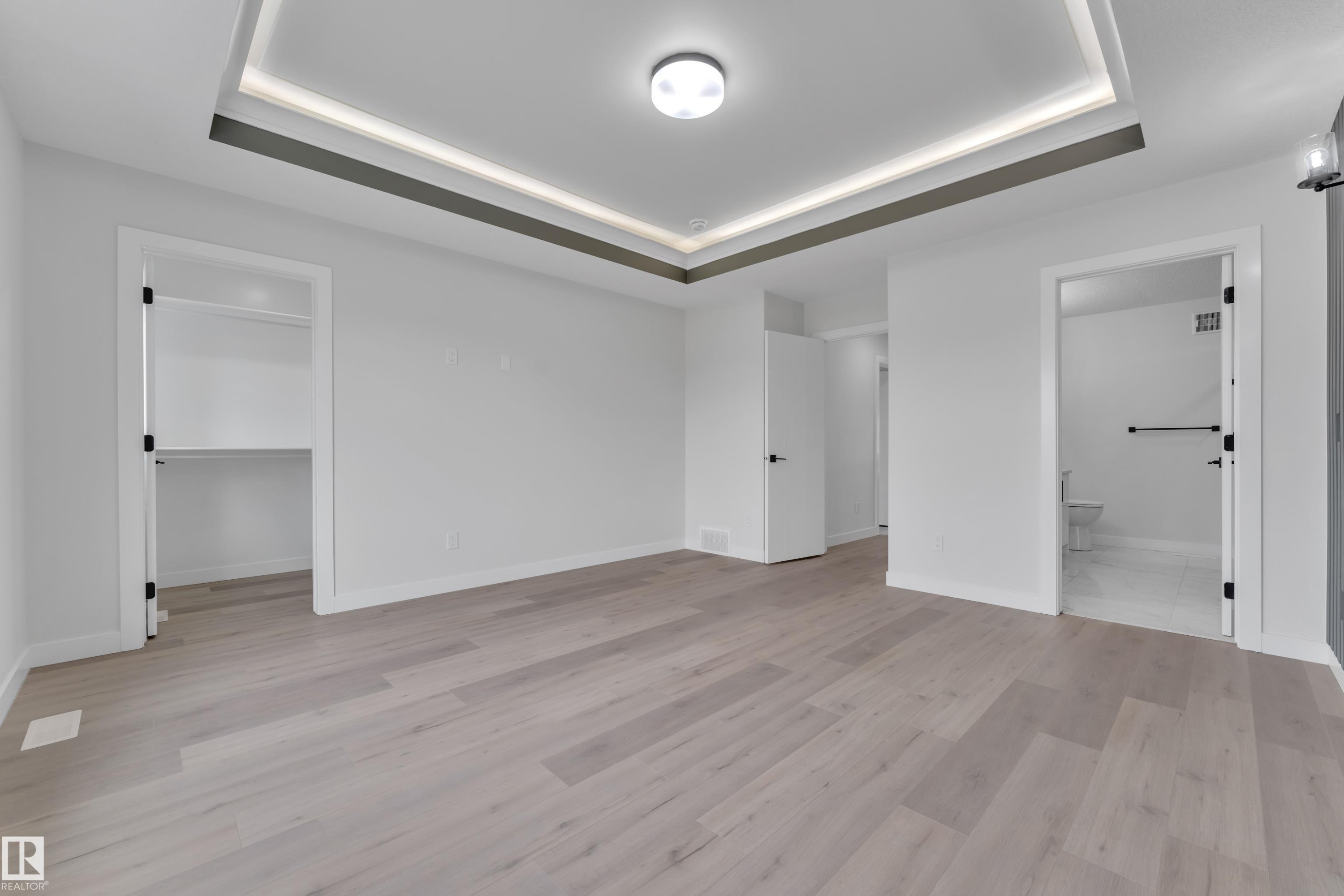 Spacious interior featuring a contemporary tray ceiling with integrated lighting, wood-finish flooring, a built-in closet, and an attached bathroom with tile flooring - 12623 44 Street, Edmonton, AB