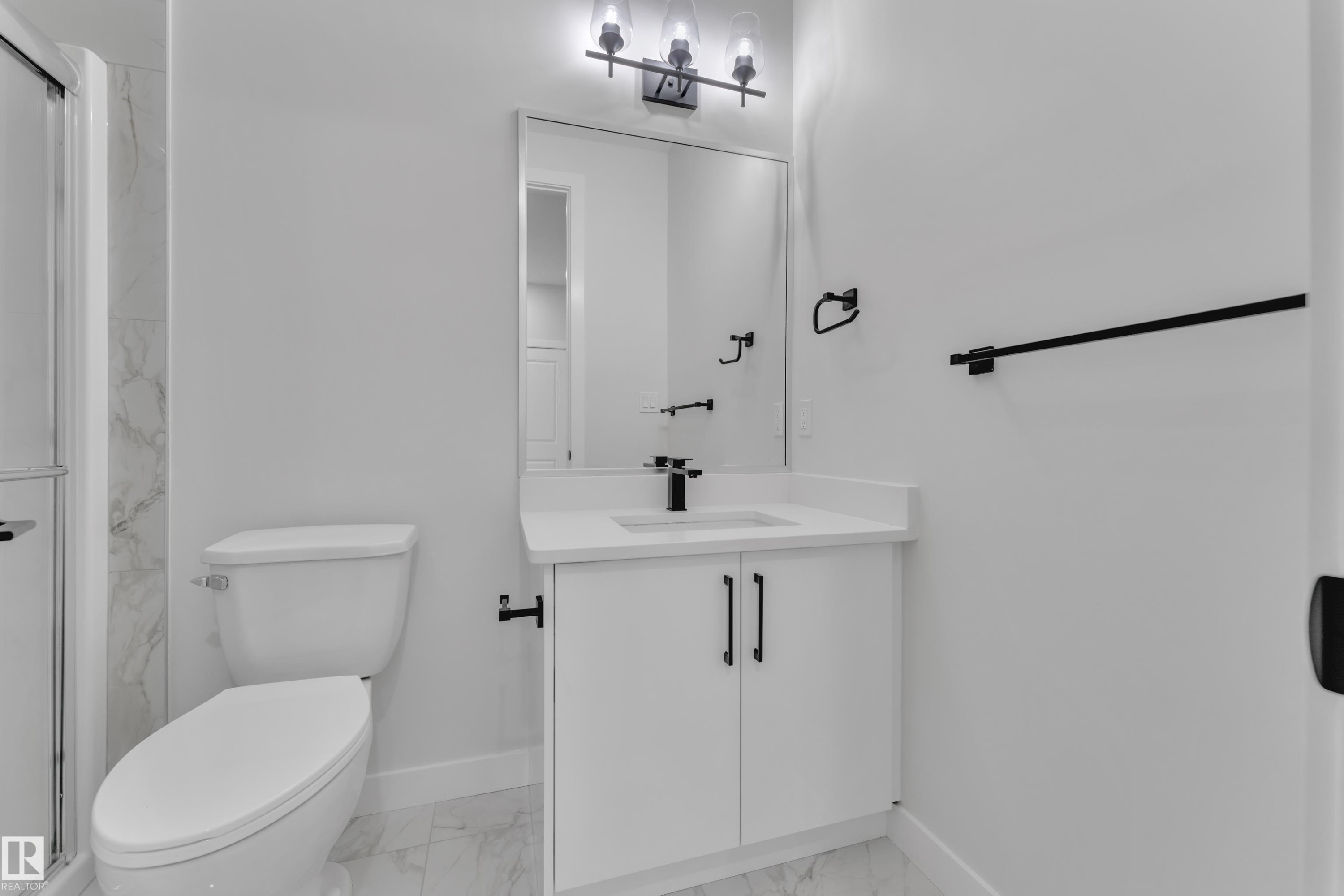 Bathroom featuring a white vanity with a single basin sink and black fixtures, a rectangular mirror, and a three-light vanity bar - 12623 44 Street, Edmonton, AB