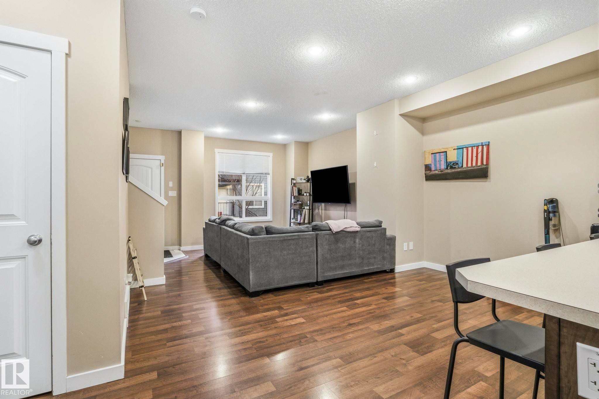 Open-concept living area featuring wood-finish flooring, recessed lighting, and neutral wall tones - 30 6075 Schonsee Way, Edmonton, AB - Indoor