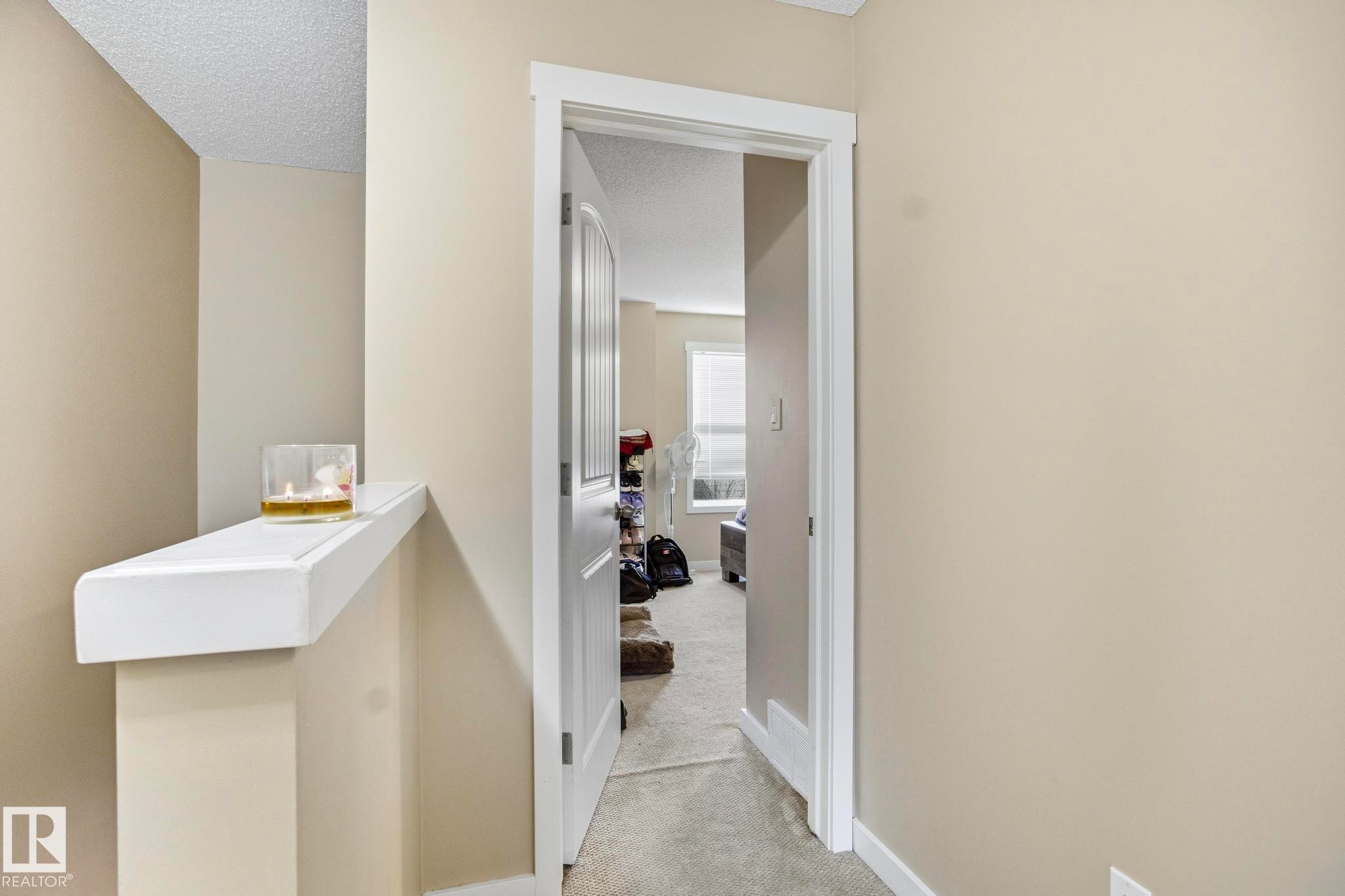 Doorway with white trim opening into a carpeted room featuring a window with horizontal blinds - 30 6075 Schonsee Way, Edmonton, AB - Indoor Photo Showing Other Room