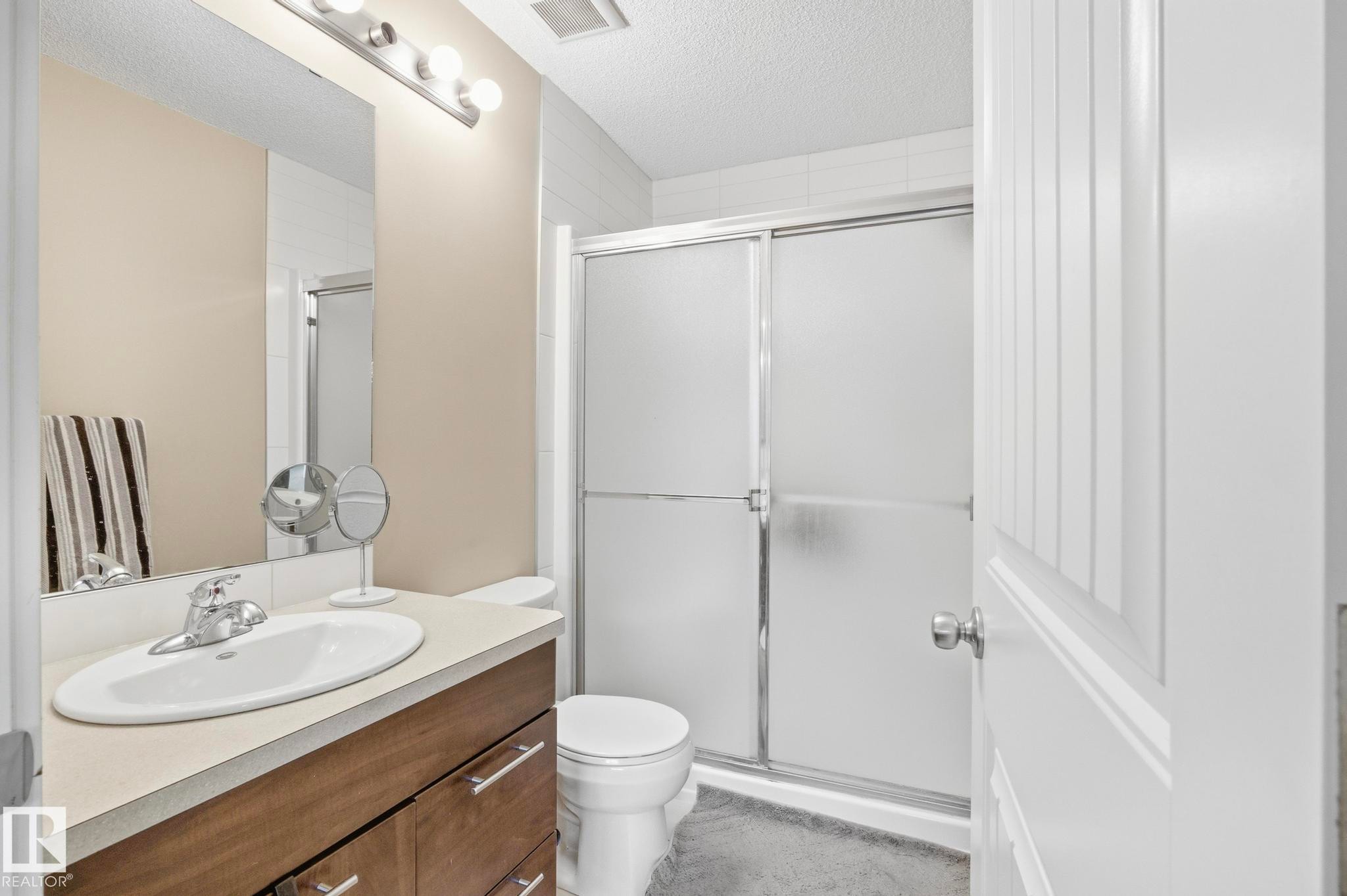Bathroom featuring a frosted glass shower enclosure, a vanity with a laminate countertop, and a large wall-mounted mirror - 30 6075 Schonsee Way, Edmonton, AB - Indoor Photo Showing Bathroom