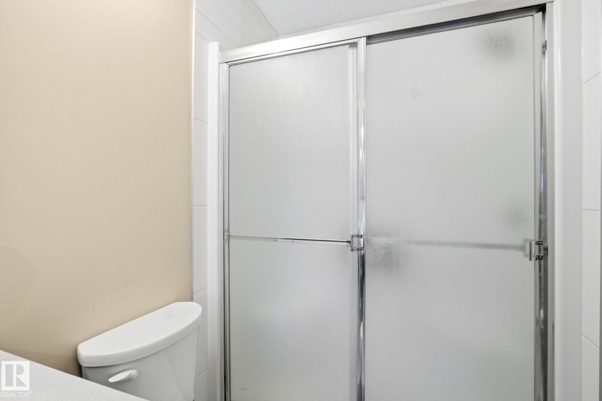 Shower enclosure with frosted glass sliding doors and a chrome frame - 30 6075 Schonsee Way, Edmonton, AB - Indoor Photo Showing Bathroom