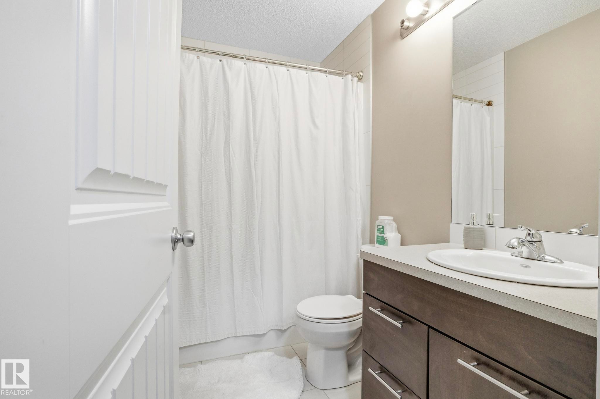 Full bathroom featuring a wood-finish vanity with a light countertop, an oval undermount sink, and a chrome faucet - 30 6075 Schonsee Way, Edmonton, AB - Indoor Photo Showing Bathroom