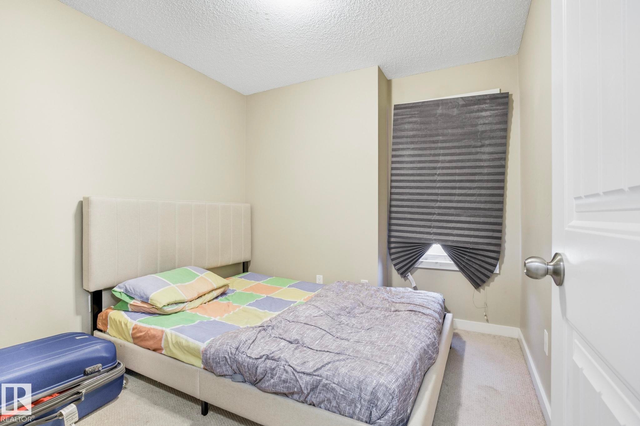 Neutral wall paint, textured ceiling, and a window with pleated blinds - 30 6075 Schonsee Way, Edmonton, AB - Indoor Photo Showing Bedroom