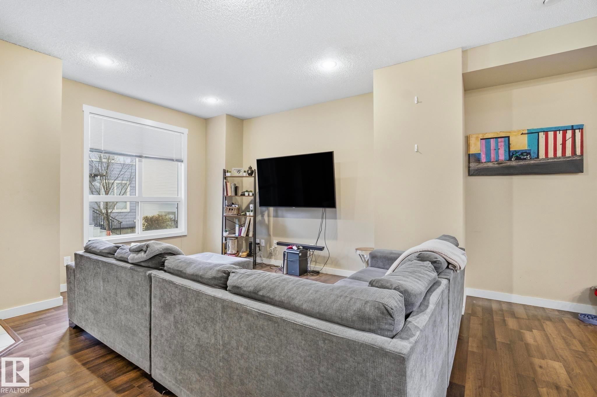 Living area featuring wood-finish flooring, a large window with white trim, recessed lighting, and neutral wall tones - 30 6075 Schonsee Way, Edmonton, AB - Indoor