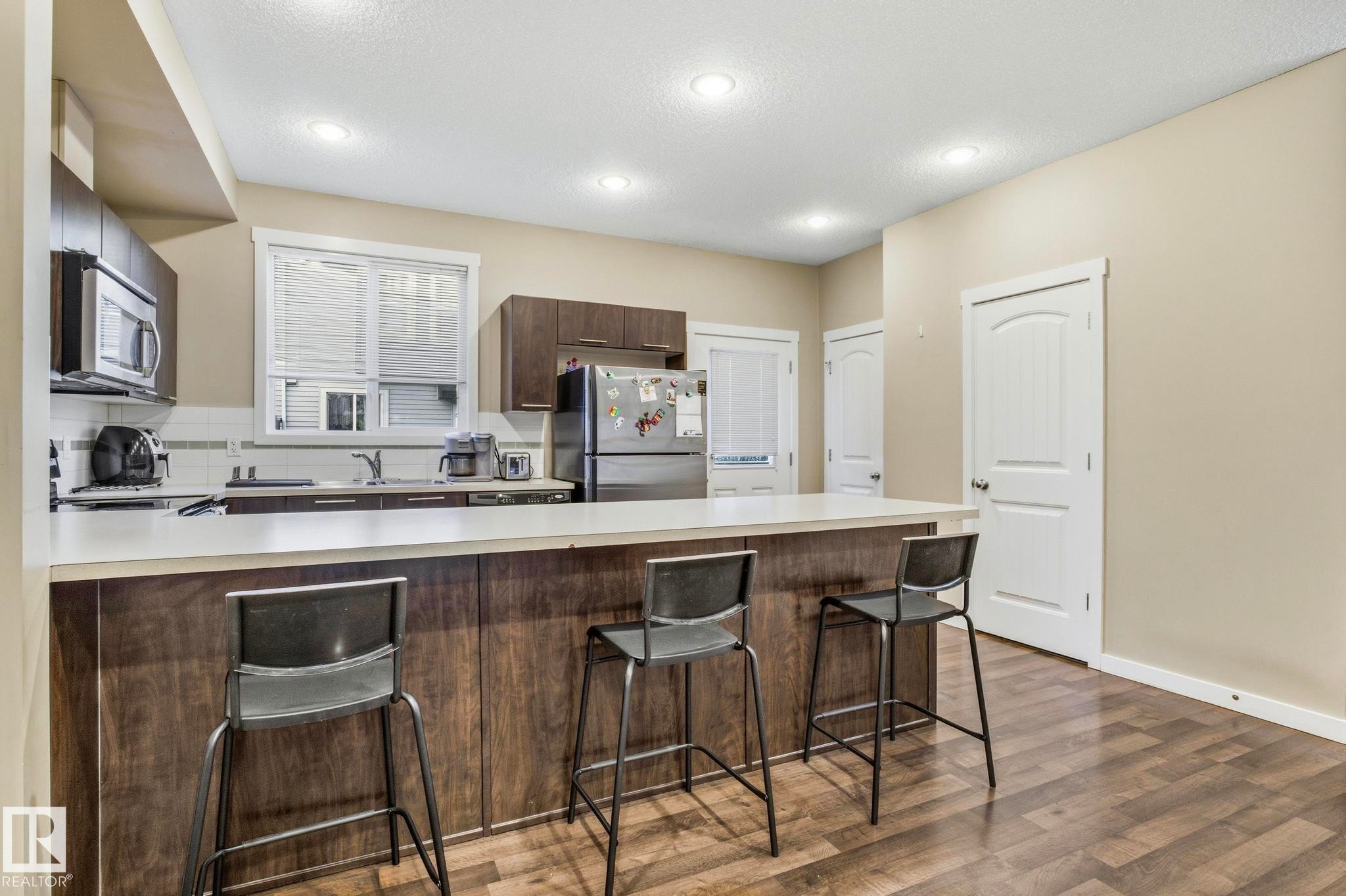 Kitchen featuring a breakfast bar with counter seating, stainless steel appliances, dark wood-finish cabinetry, and wood-finish flooring - 30 6075 Schonsee Way, Edmonton, AB - Indoor Photo Showing Kitchen