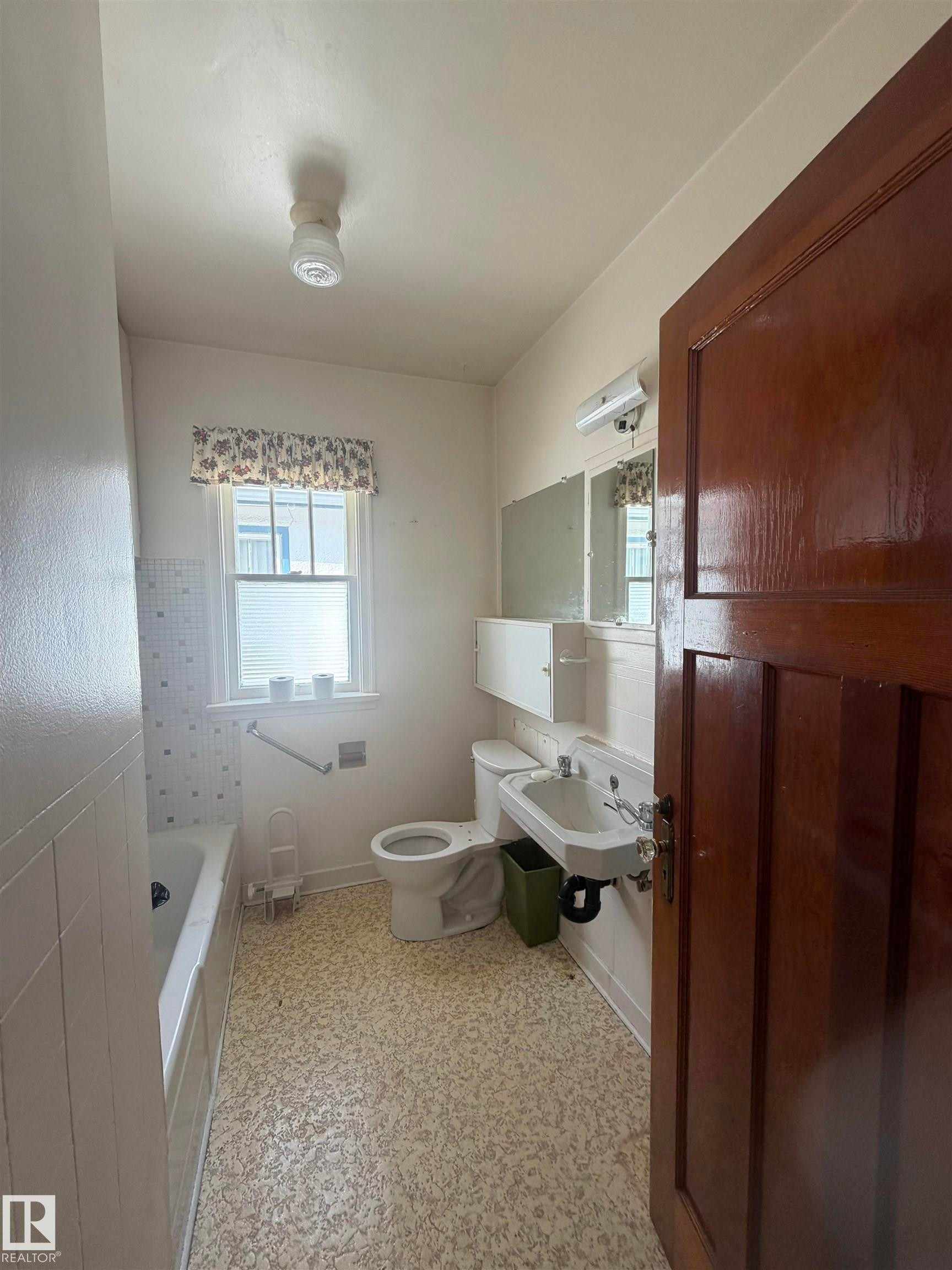 Bathroom featuring a white bathtub, wall-mounted sink, toilet, and window with patterned valance - 9630 106 Avenue, Edmonton, AB - Indoor Photo Showing Other Room