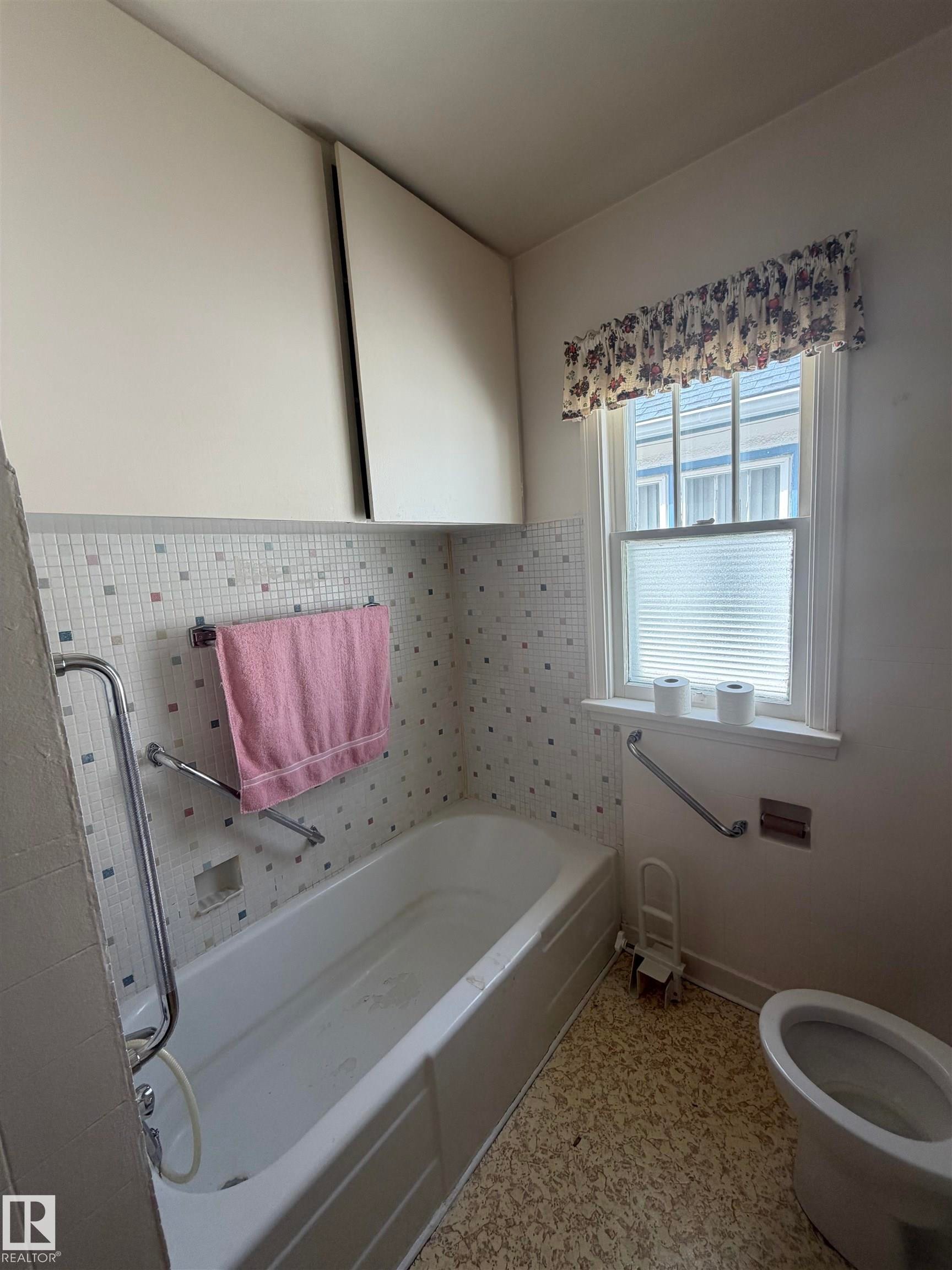 Bathroom featuring a built-in bathtub with subway tile surround, mosaic accent tiles, and two wall-mounted storage cabinets - 9630 106 Avenue, Edmonton, AB - Indoor Photo Showing Bathroom