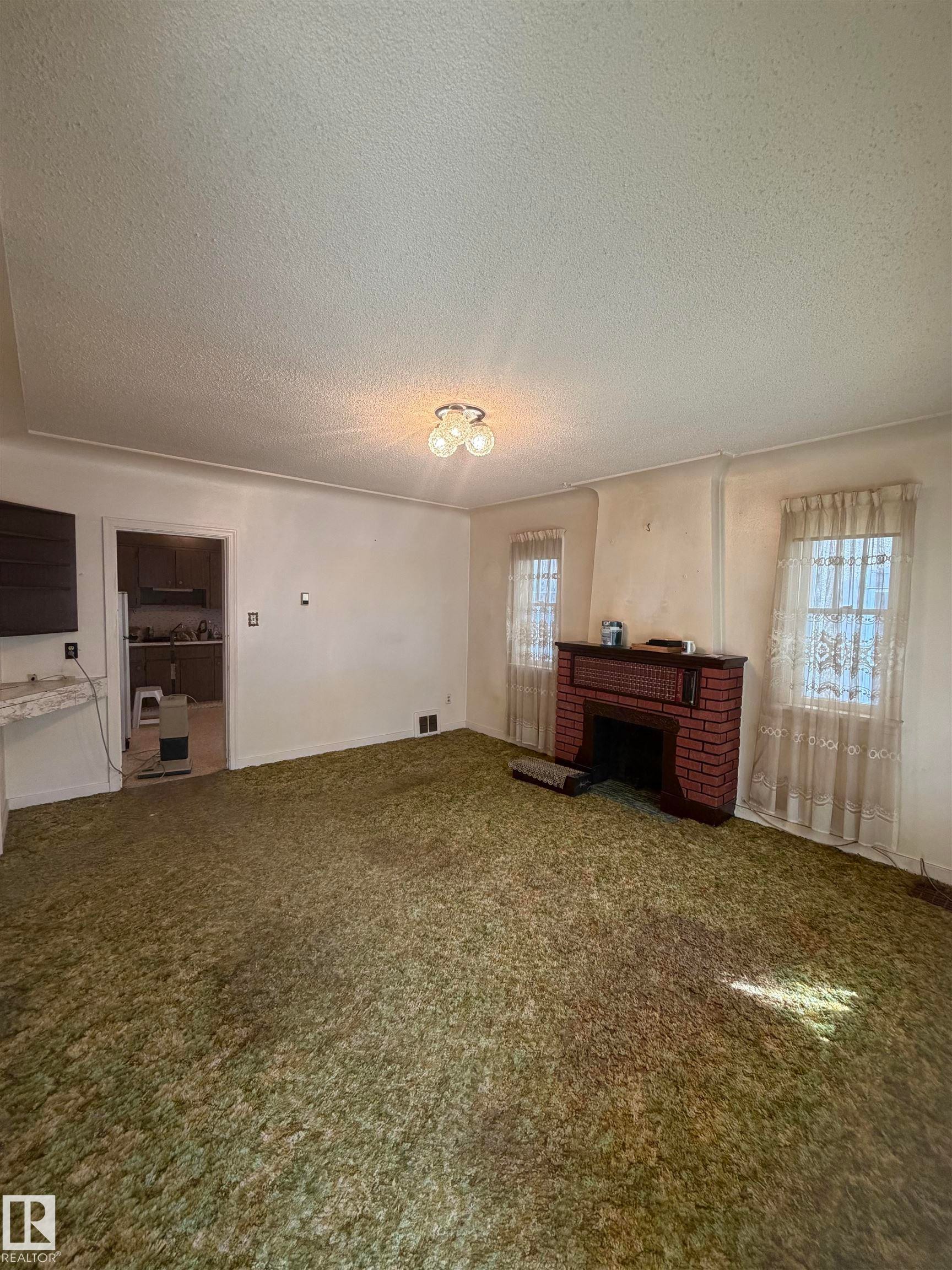 Living area featuring a brick fireplace with a dark wood mantel, two windows, and a ceiling-mounted light fixture - 9630 106 Avenue, Edmonton, AB - Indoor Photo Showing Other Room