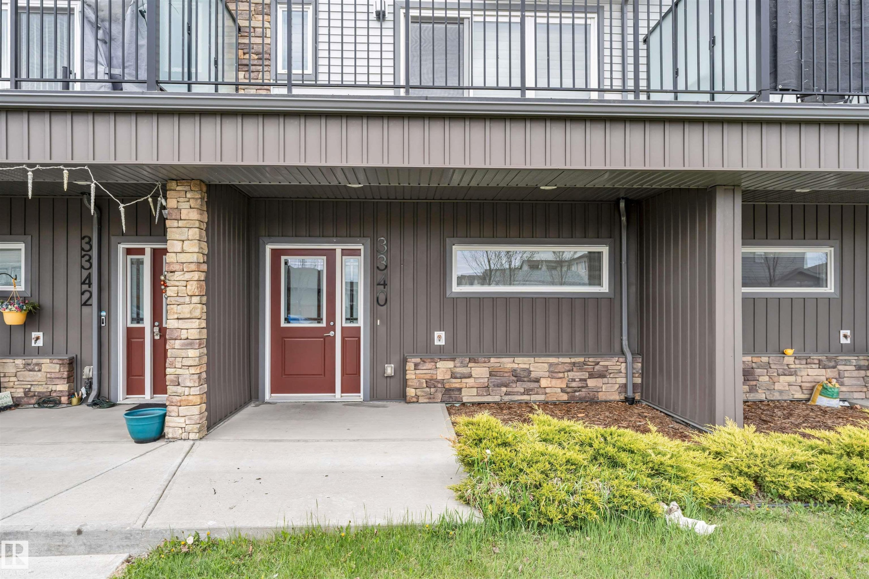 Ground-level unit featuring a rich red entry door with sidelights, composite siding, and a stone veneer accent - 3340 15A Avenue, Edmonton, AB - Outdoor
