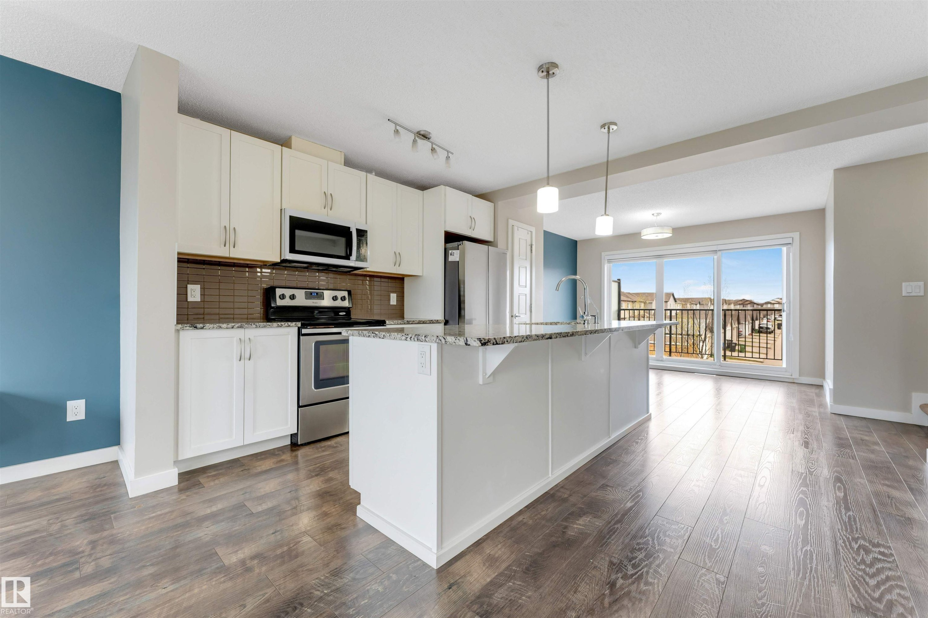 Open-concept kitchen featuring white cabinetry, stainless steel appliances, a large island with pendant lighting, and wood-finish flooring - 3340 15A Avenue, Edmonton, AB - Indoor Photo Showing Kitchen With Upgraded Kitchen