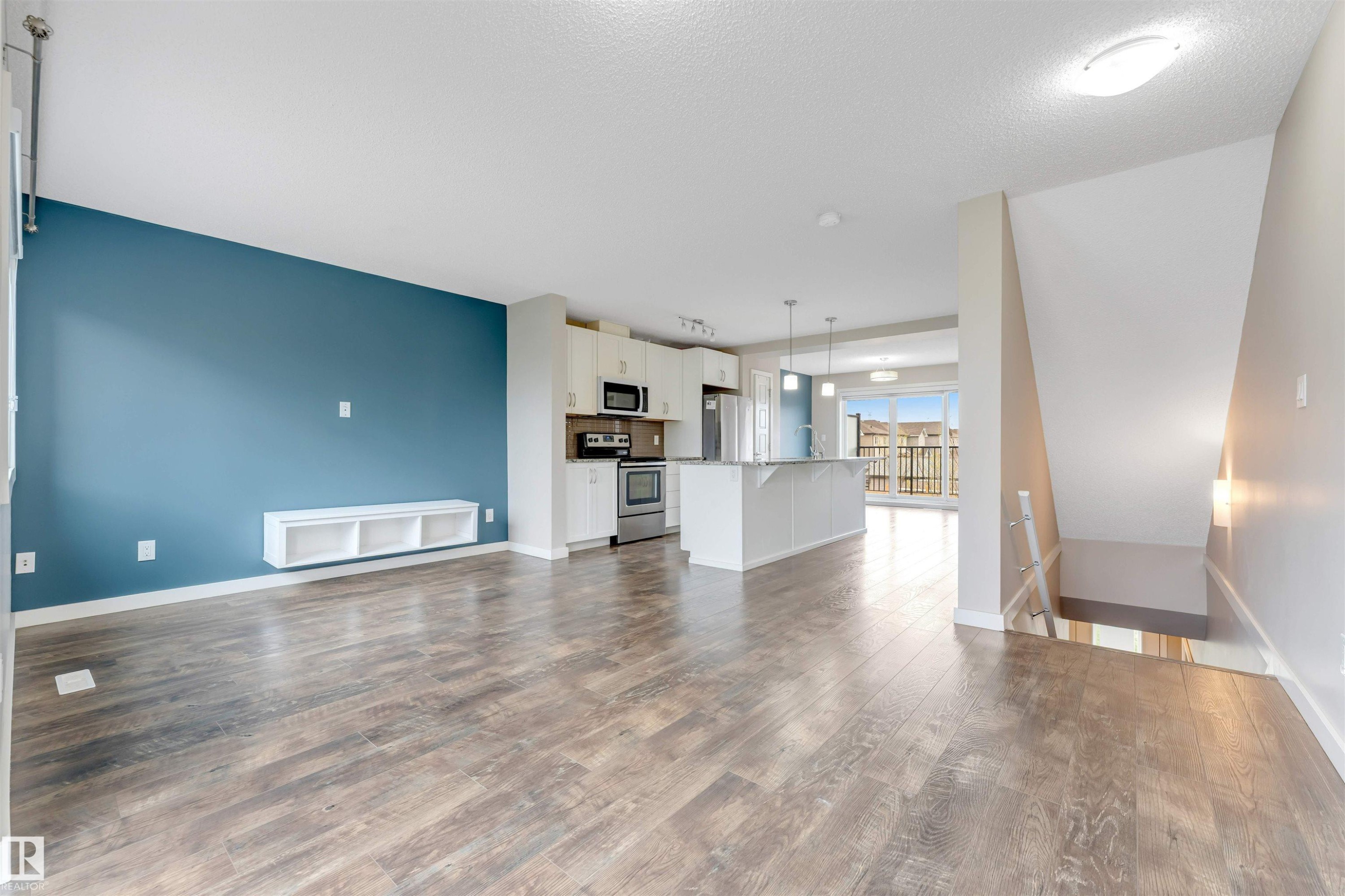 Open-concept living area with wood-finish flooring, a contemporary blue accent wall, and a built-in white shelving unit - 3340 15A Avenue, Edmonton, AB - Indoor Photo Showing Living Room