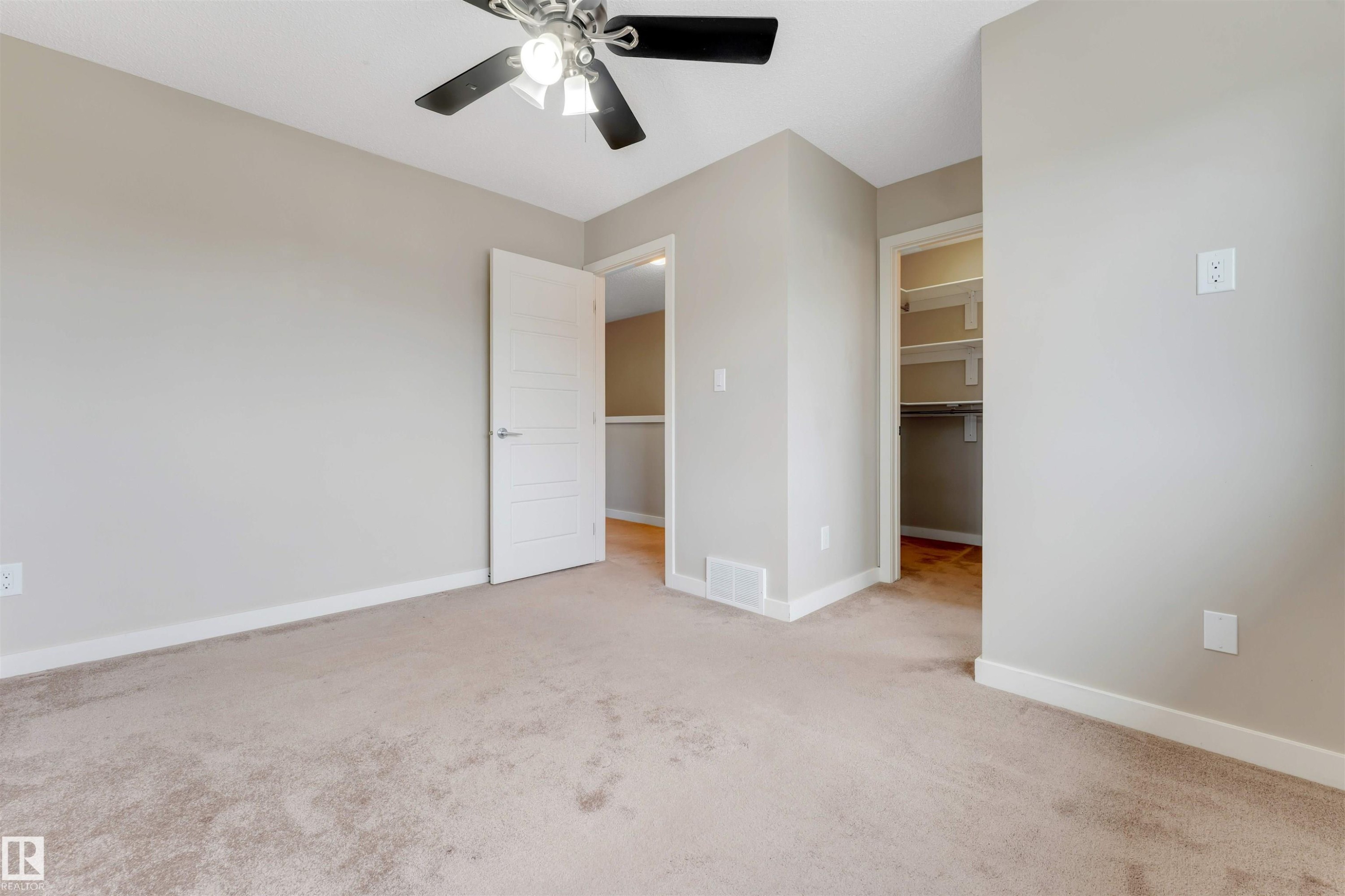 Carpeted room with neutral wall tones, a modern ceiling fan, and a walk-in closet featuring built-in shelving - 3340 15A Avenue, Edmonton, AB - Indoor Photo Showing Other Room