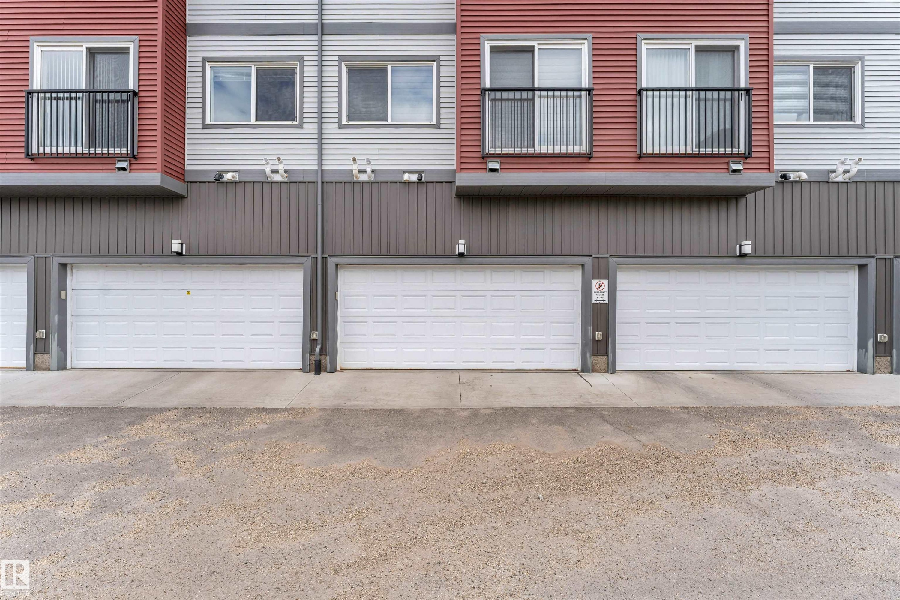 Exterior facade featuring horizontal siding in red and grey tones, multiple white paneled garage doors, and balconies with black railings - 3340 15A Avenue, Edmonton, AB - With Exterior