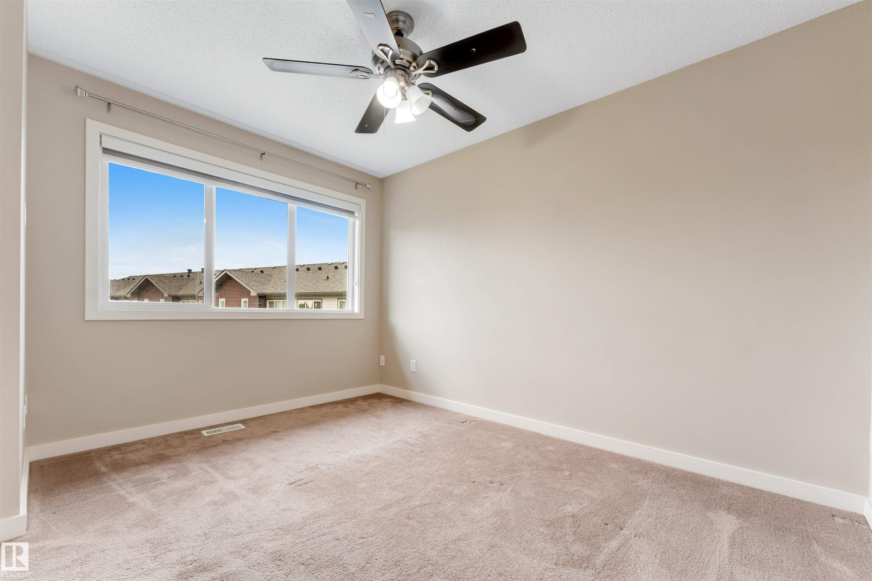 Carpeted room featuring a large window, a ceiling fan with integrated lighting, and neutral wall tones - 3340 15A Avenue, Edmonton, AB - Indoor Photo Showing Other Room