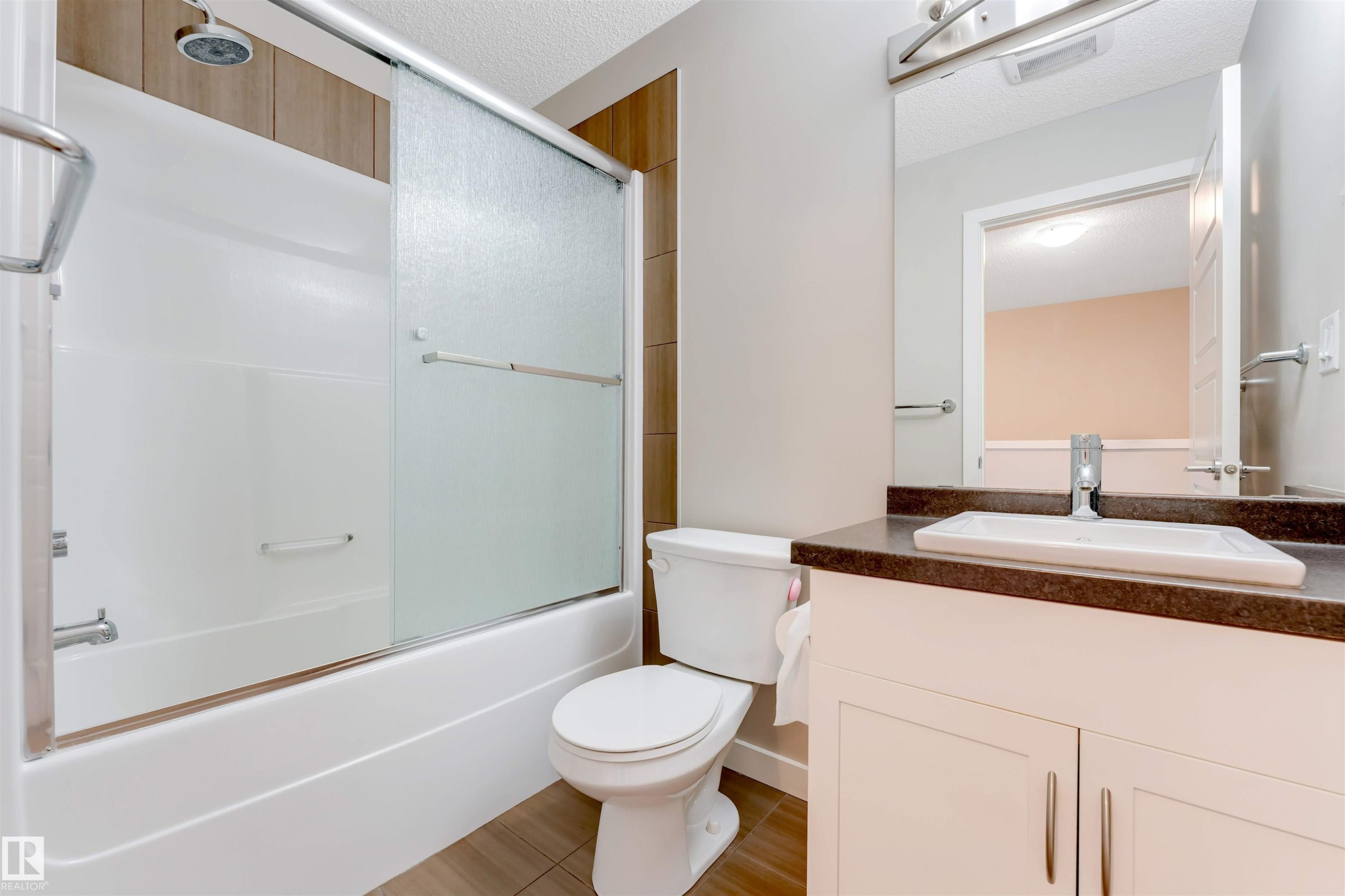Bathroom featuring a white bathtub with frosted sliding doors, a shower head, and a toilet - 3340 15A Avenue, Edmonton, AB - Indoor Photo Showing Bathroom