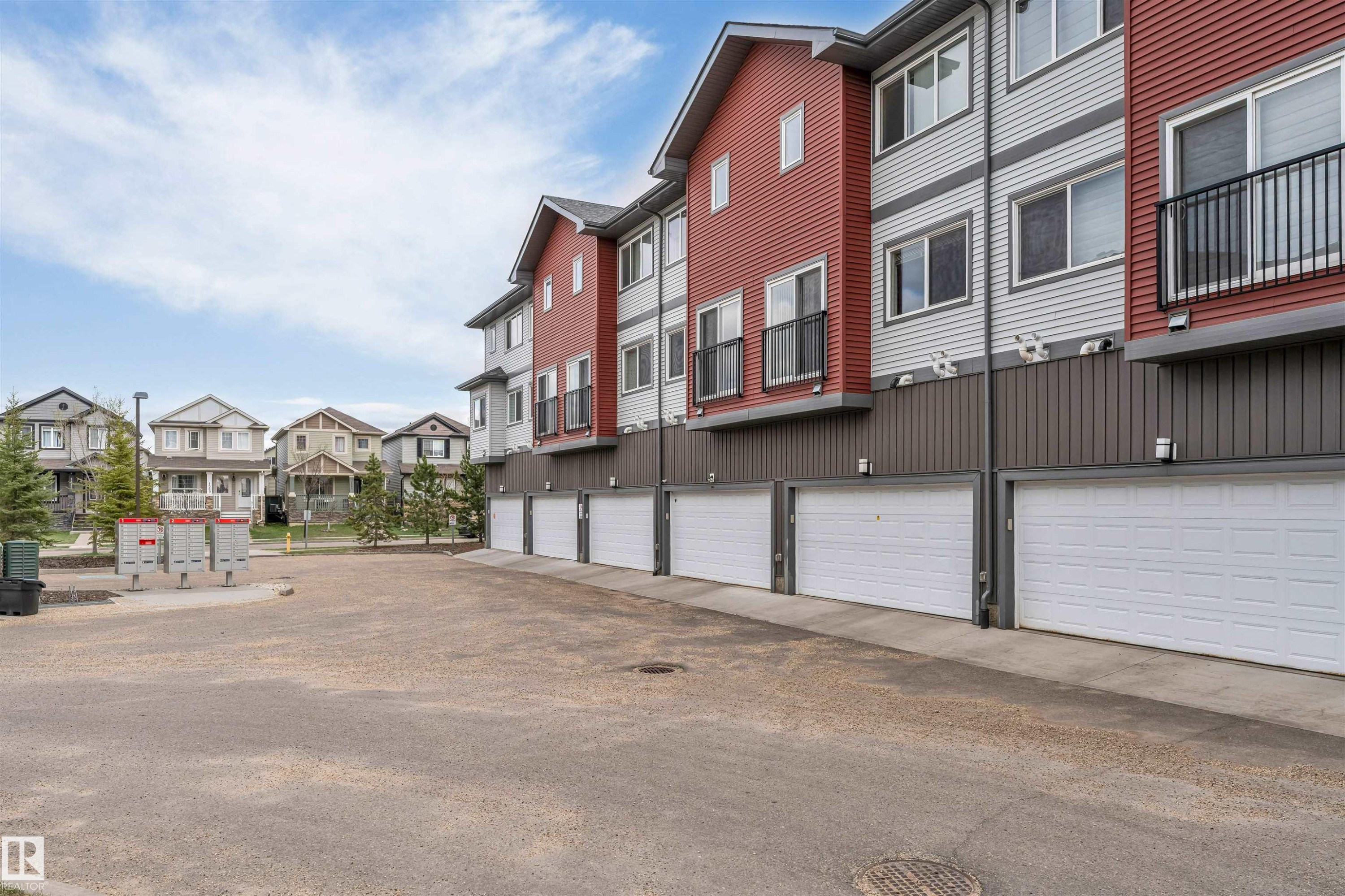 Multi-story townhomes with red and grey panel siding, individual garage doors, and private balconies with black railings - 3340 15A Avenue, Edmonton, AB - Outdoor