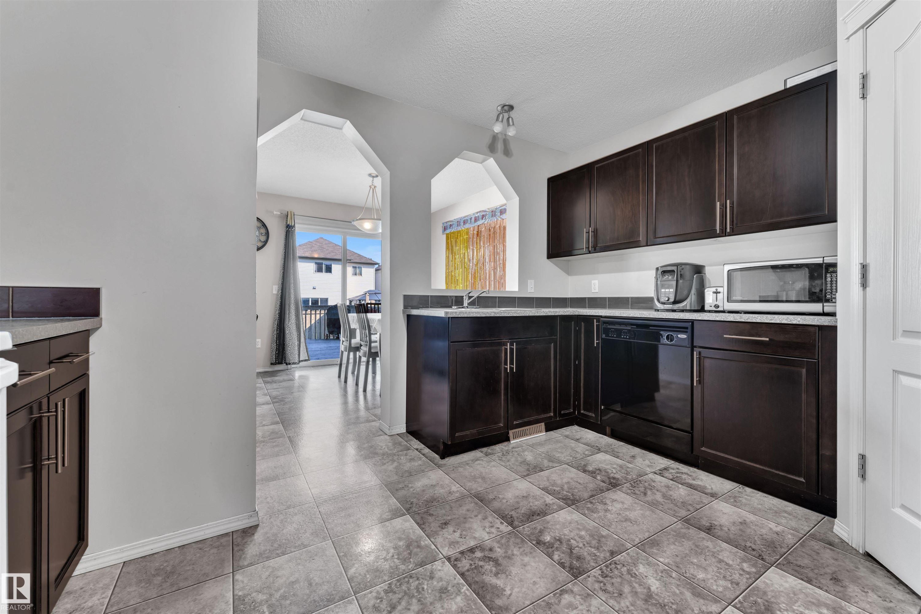 Kitchen featuring dark brown cabinetry, arched walkways, a textured ceiling, dishwasher, and light countertops - 6152 13 Avenue, Edmonton, AB - Indoor Photo Showing Kitchen