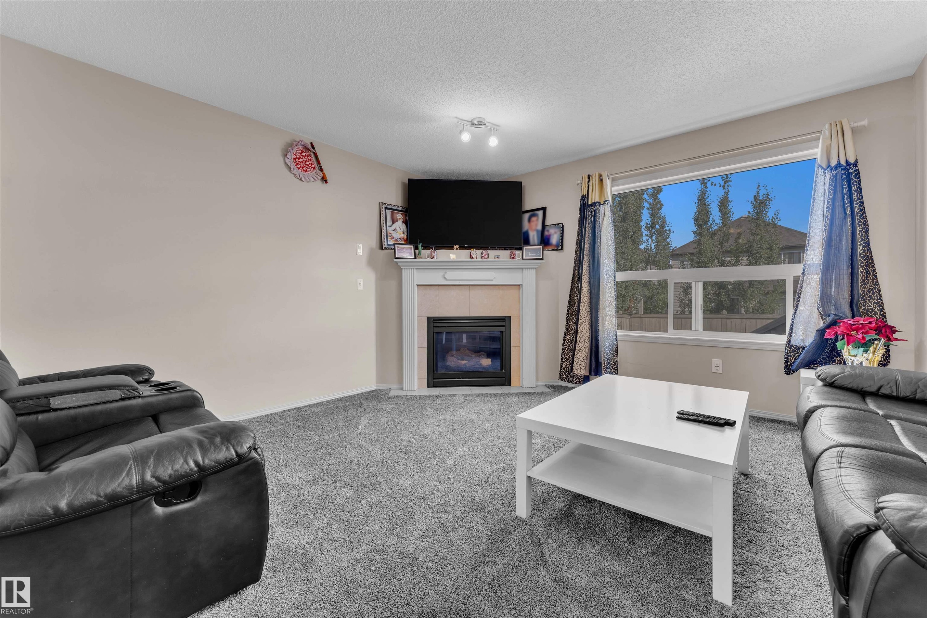 Living area with carpet flooring, a tile fireplace, and a textured ceiling - 6152 13 Avenue, Edmonton, AB - Indoor Photo Showing Living Room With Fireplace