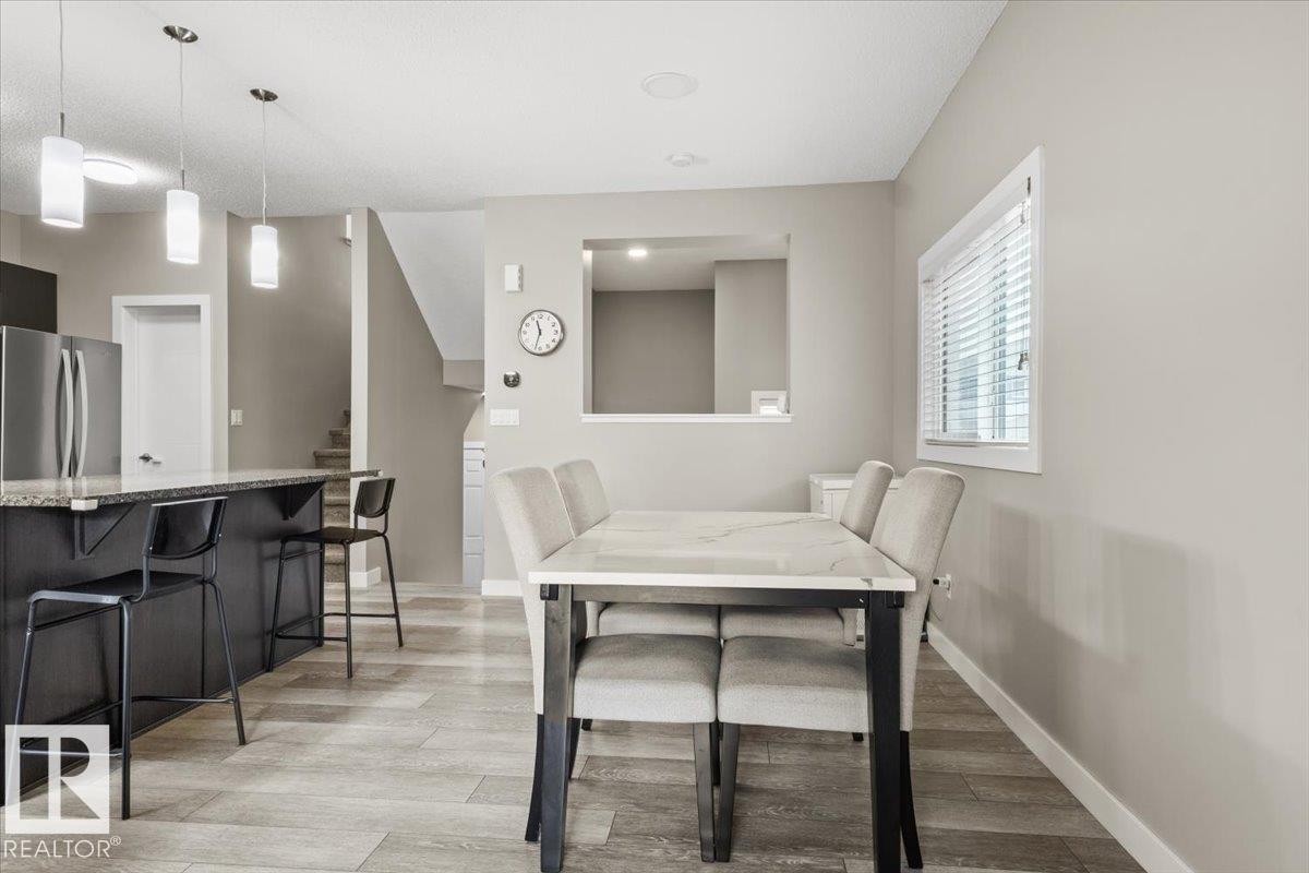 Open-concept living space featuring wood-finish flooring, a kitchen island with stone countertop, stainless steel appliances, a dining area, and a window with blinds - 236 39 Avenue, Edmonton, AB - Indoor Photo Showing Dining Room
