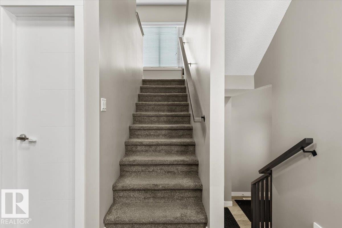 Carpeted staircase featuring a window with blinds, a modern white door with horizontal paneling, and dark handrails - 236 39 Avenue, Edmonton, AB - Indoor Photo Showing Other Room