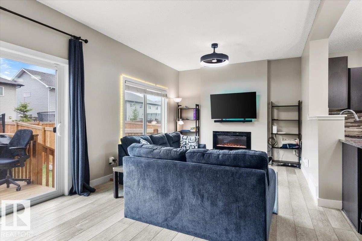 Living area featuring wood-finish flooring, a contemporary electric fireplace, and a glass sliding door providing outdoor access to a private wooden deck - 236 39 Avenue, Edmonton, AB - Indoor Photo Showing Living Room With Fireplace
