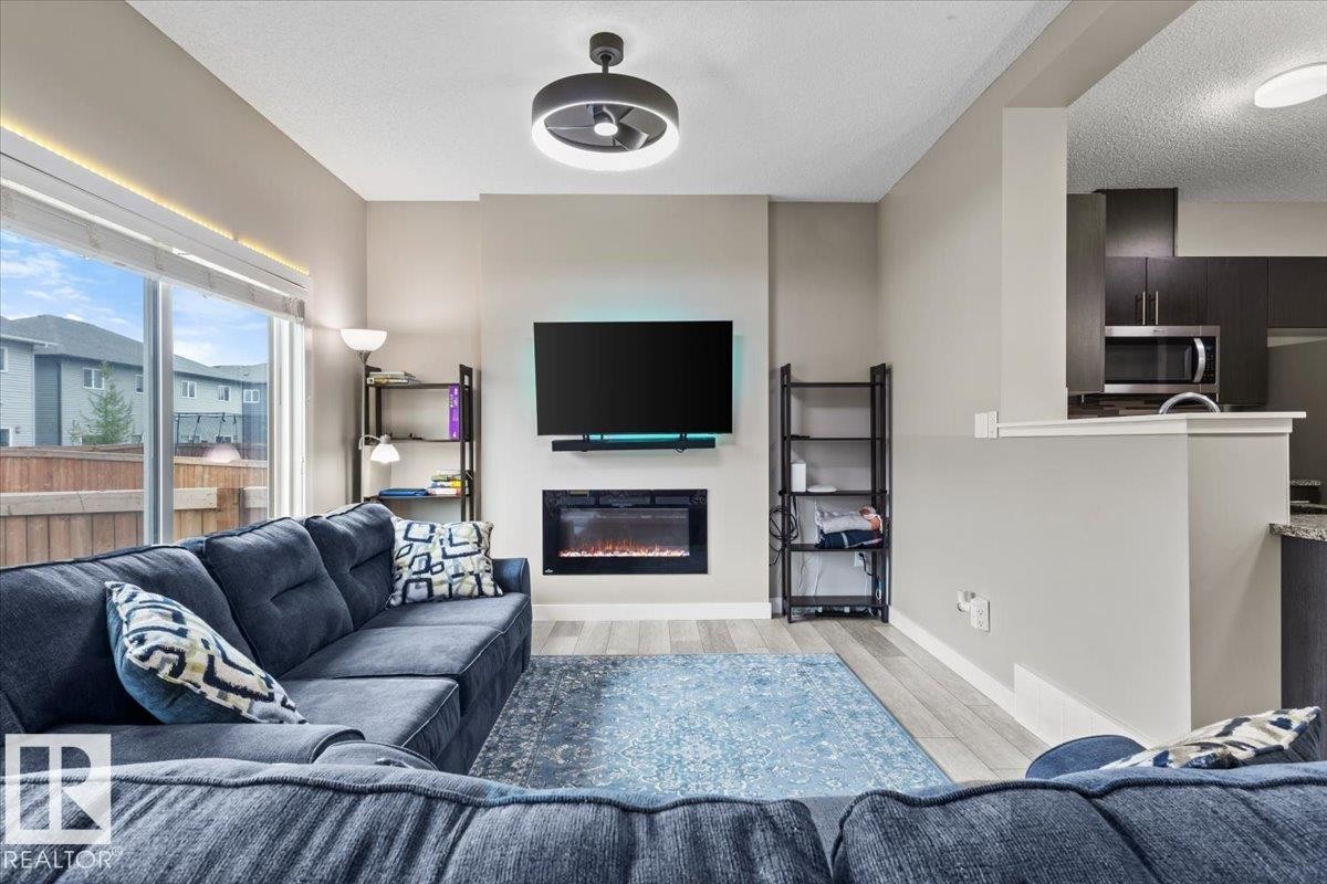 Living area featuring a modern electric fireplace, wall-mounted television, and wood-finish flooring - 236 39 Avenue, Edmonton, AB - Indoor Photo Showing Living Room With Fireplace