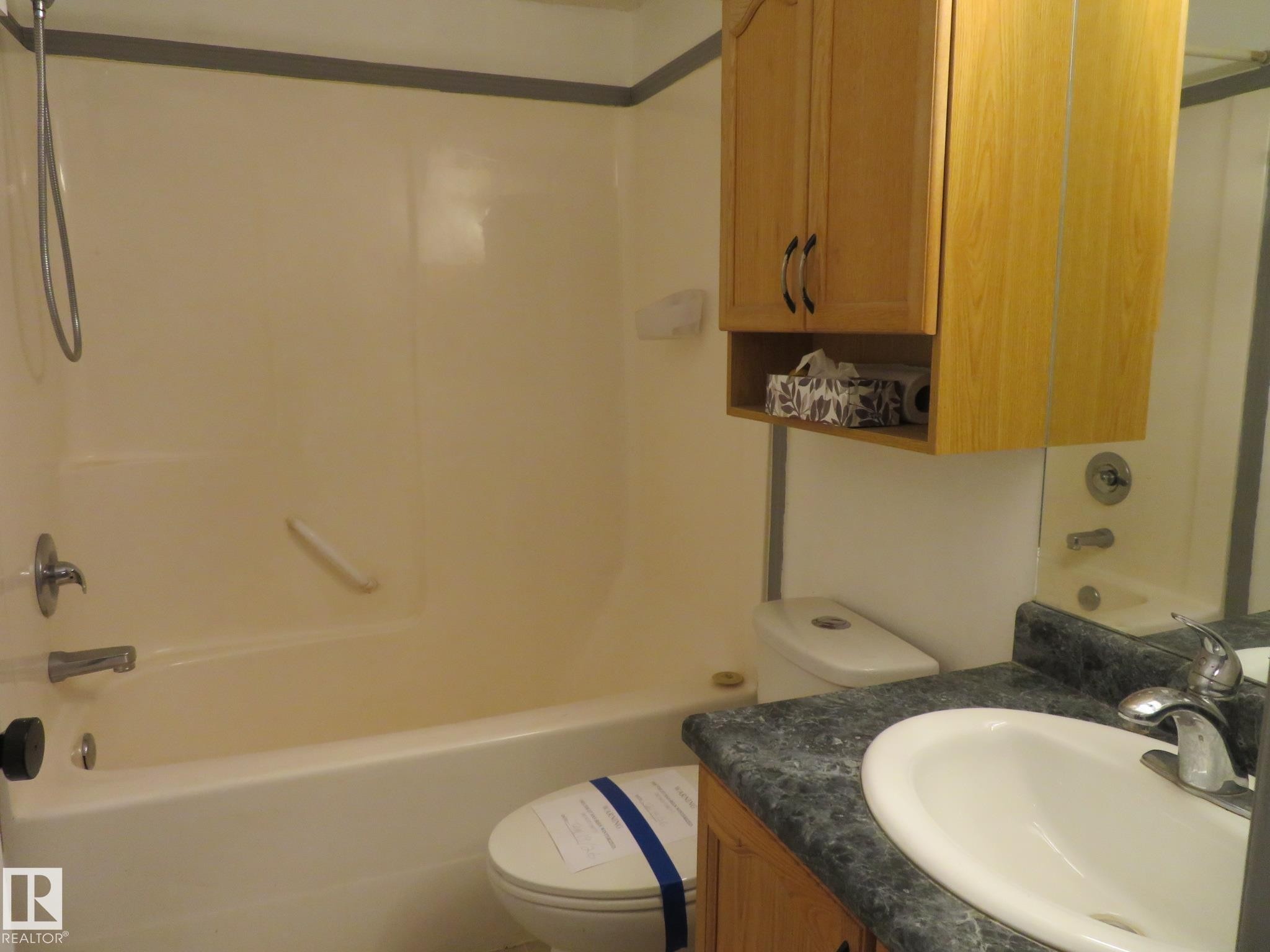 Bathroom featuring a built-in tub with shower, a vanity with an integrated sink, a dark speckled countertop, and natural wood-finish cabinetry - 2945 26 Street, Edmonton, AB - Indoor Photo Showing Bathroom