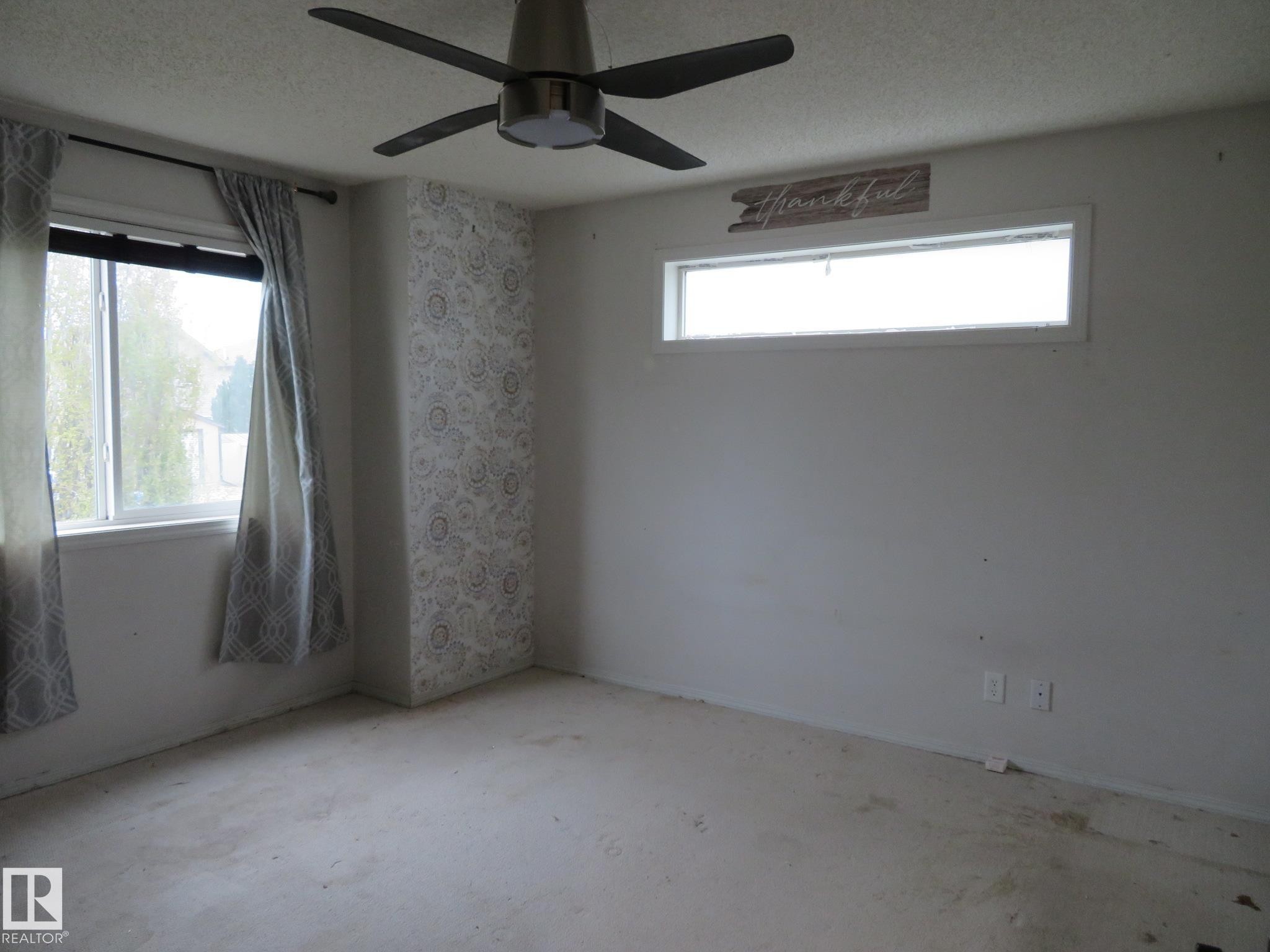 Spacious room featuring a ceiling fan with integrated lighting, two window openings, and a decorative accent wall with patterned wallpaper - 2945 26 Street, Edmonton, AB - Indoor