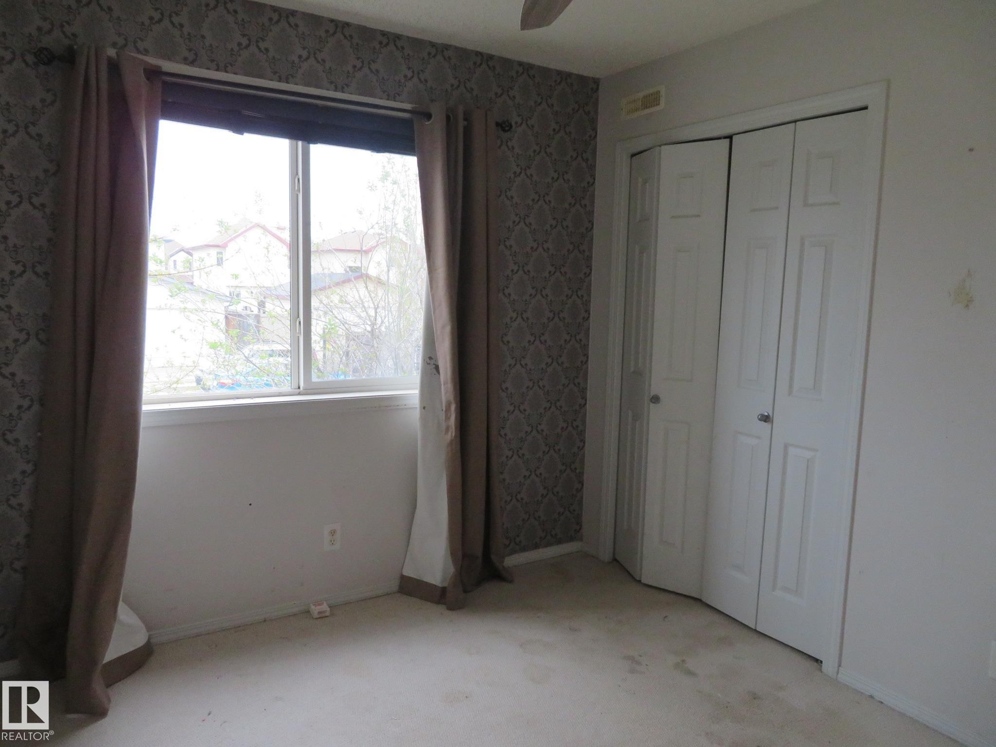Windowed room featuring a patterned accent wall, light-toned carpeting, and bi-fold closet doors - 2945 26 Street, Edmonton, AB - Indoor