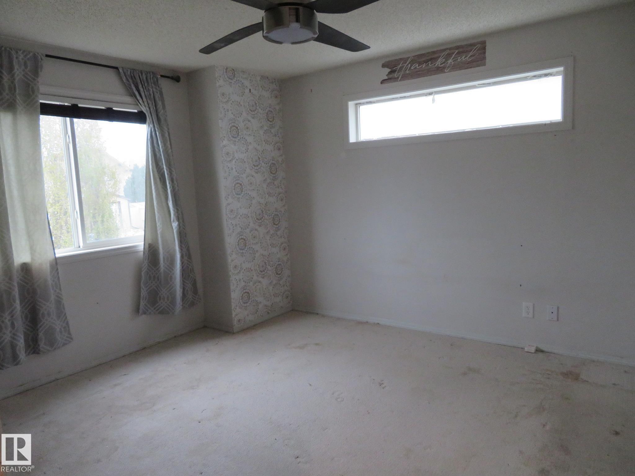 Spacious room featuring a ceiling fan, two windows for natural light, and a patterned accent wall - 2945 26 Street, Edmonton, AB - Indoor