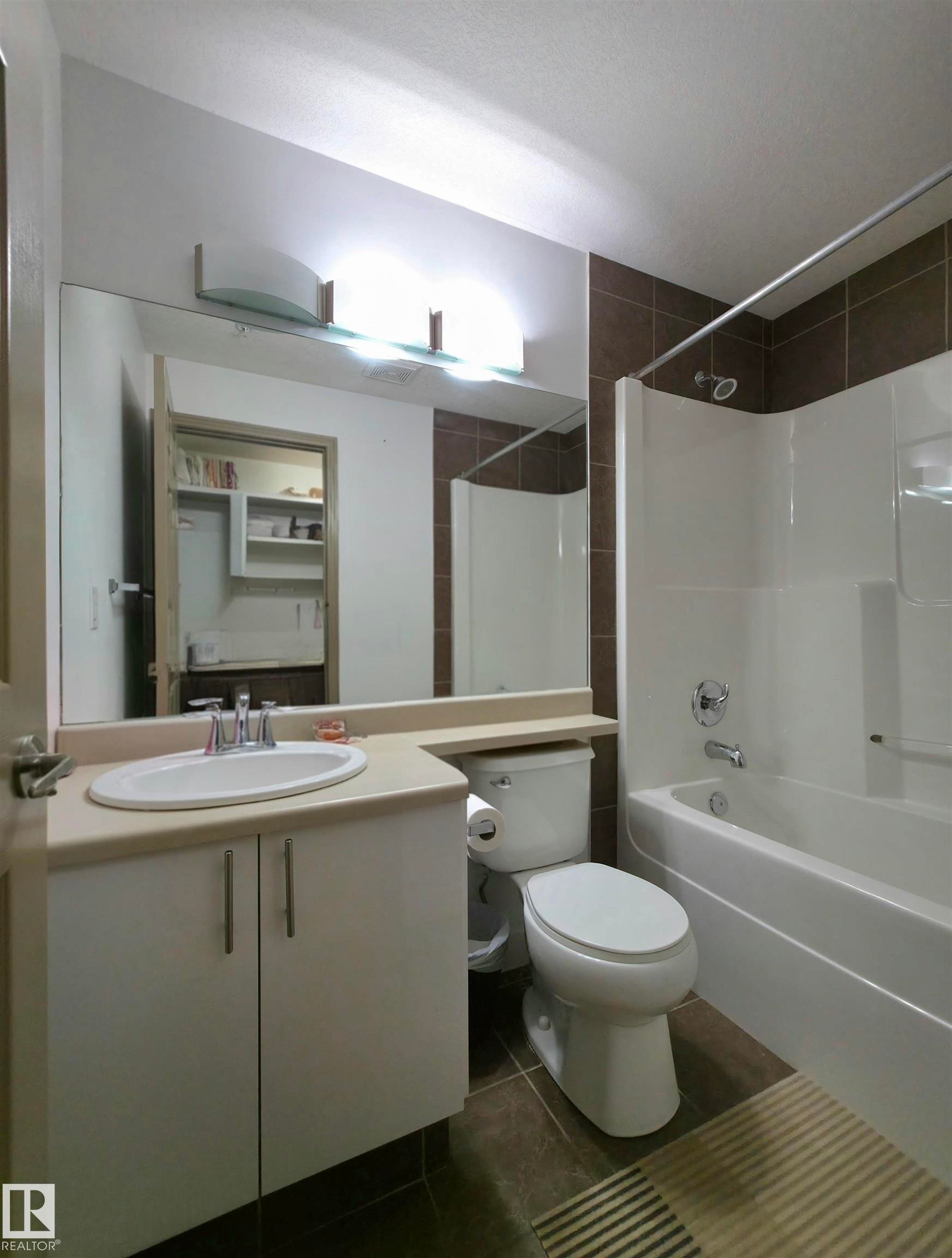 Bathroom featuring a white vanity with an integrated sink, polished chrome faucet, and expansive mirror - 210 5005 165 Avenue, Edmonton, AB - Indoor Photo Showing Bathroom