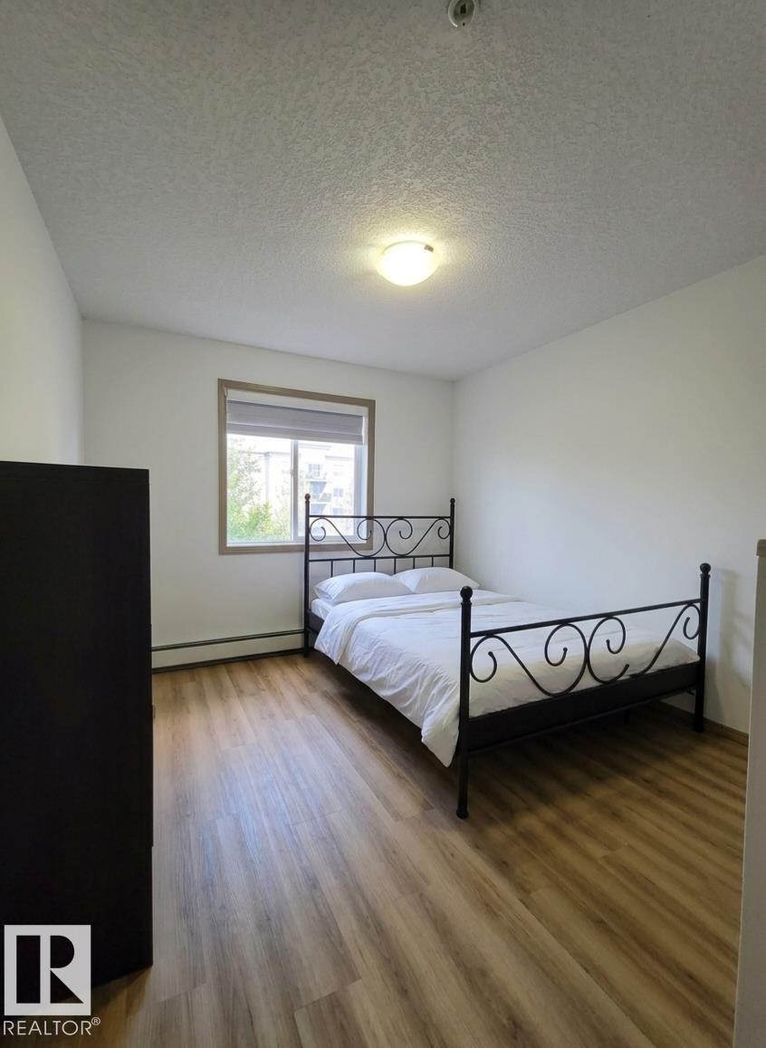 Room featuring wood-finish flooring, a window with a neutral blind, and a ceiling-mounted light fixture - 210 5005 165 Avenue, Edmonton, AB - Indoor Photo Showing Bedroom