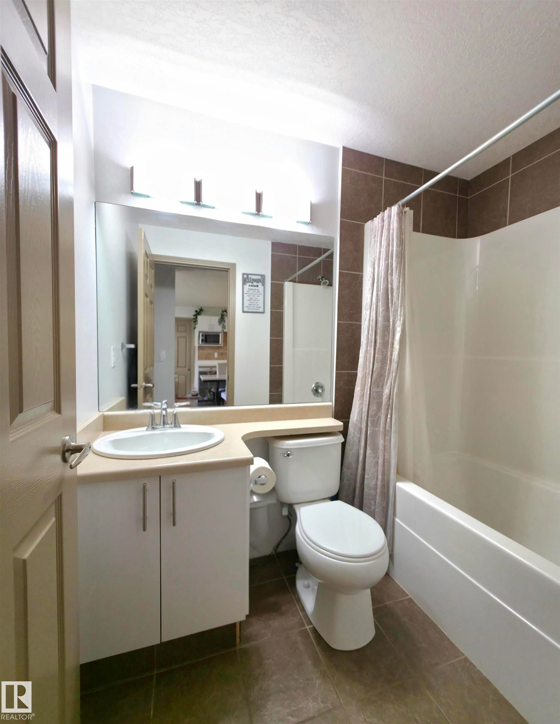 Bathroom with a white vanity featuring a single basin sink, a large wall-mounted mirror, and a three-light fixture - 210 5005 165 Avenue, Edmonton, AB - Indoor Photo Showing Bathroom