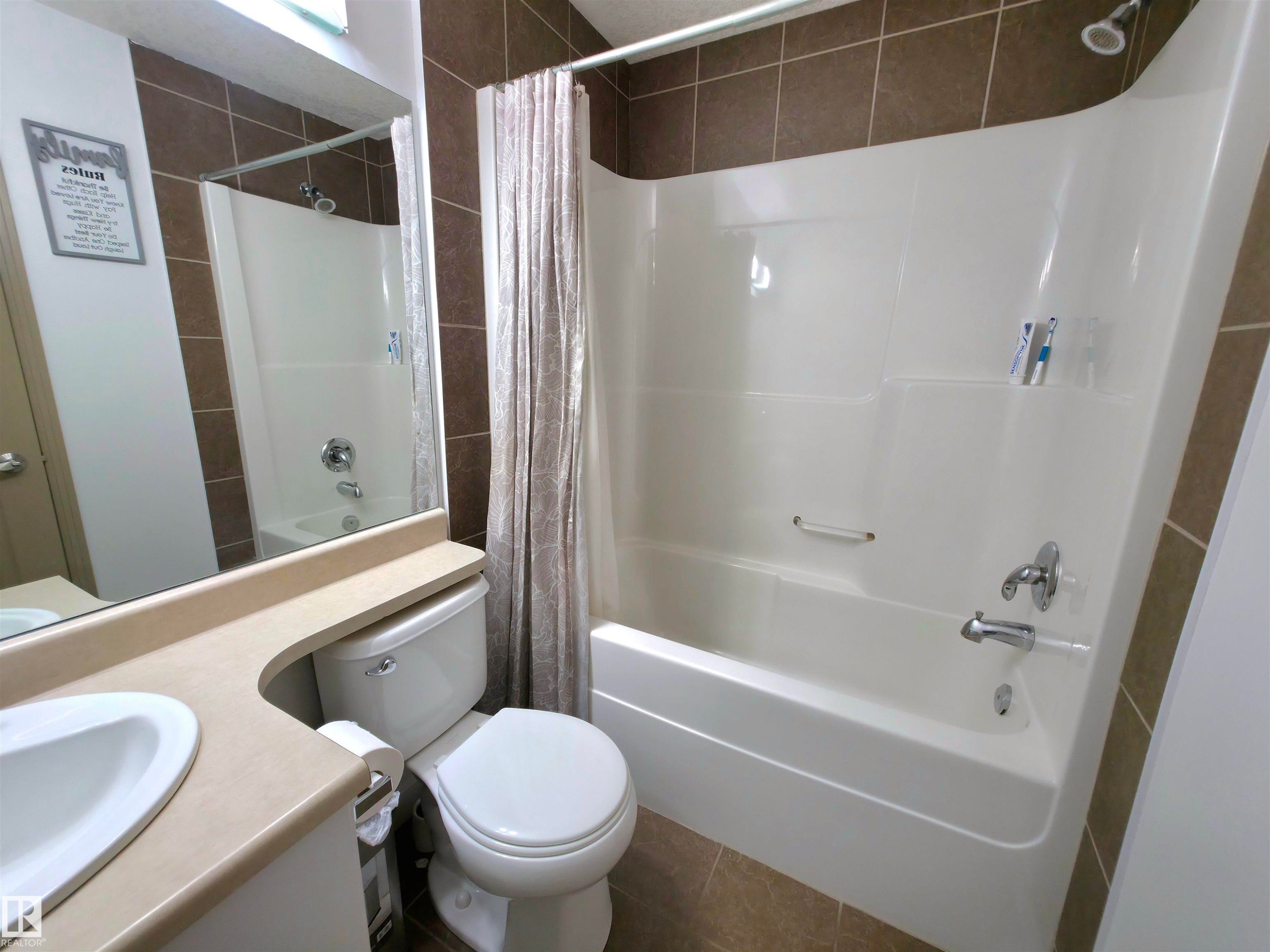 Full bathroom featuring a white tub/shower combination with chrome fixtures, a single vanity with an integrated sink, and a toilet - 210 5005 165 Avenue, Edmonton, AB - Indoor Photo Showing Bathroom
