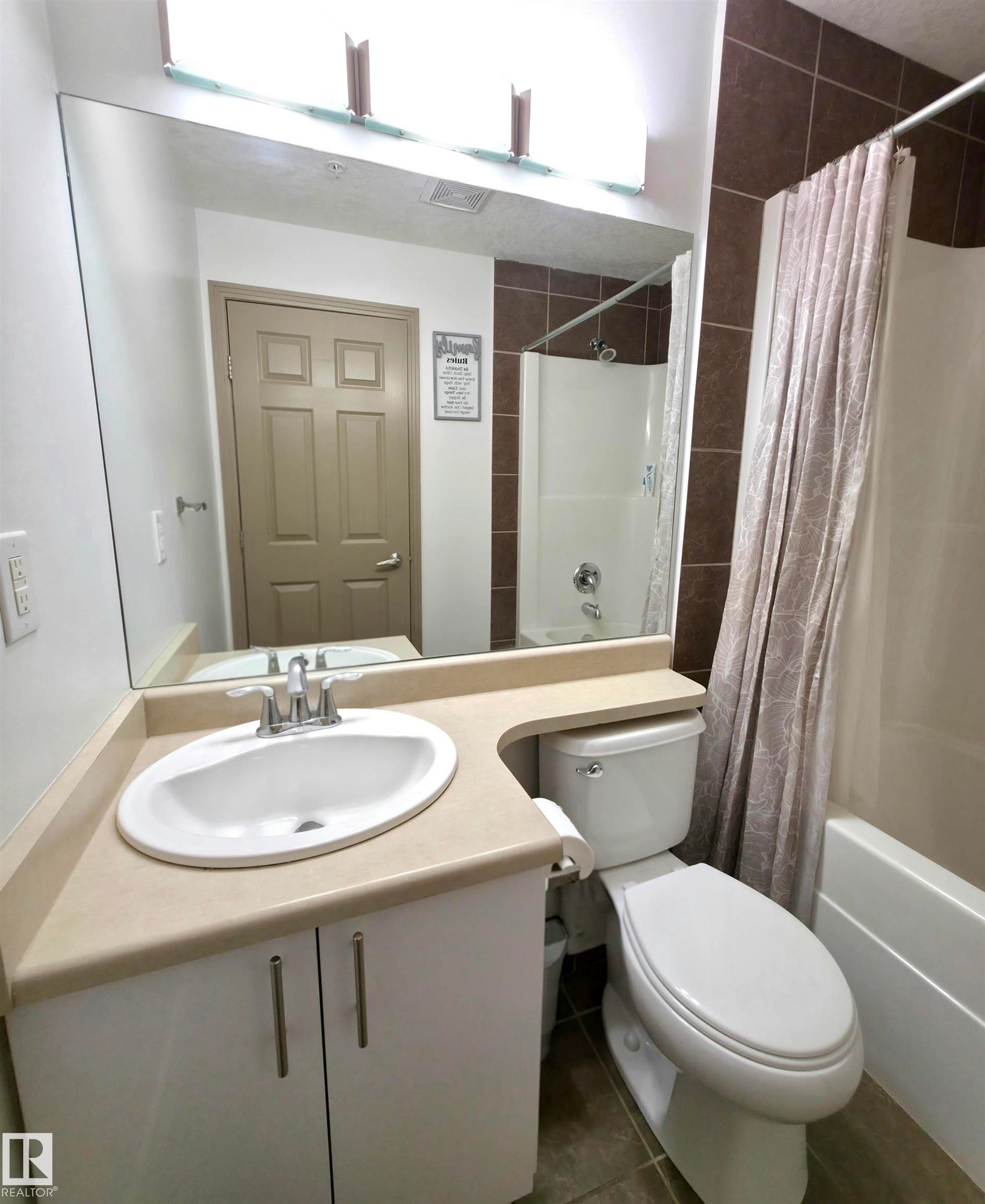 Full bathroom featuring a single vanity with an integrated sink, a large wall-mounted mirror, a toilet, and a combined tub and shower with tile surround - 210 5005 165 Avenue, Edmonton, AB - Indoor Photo Showing Bathroom