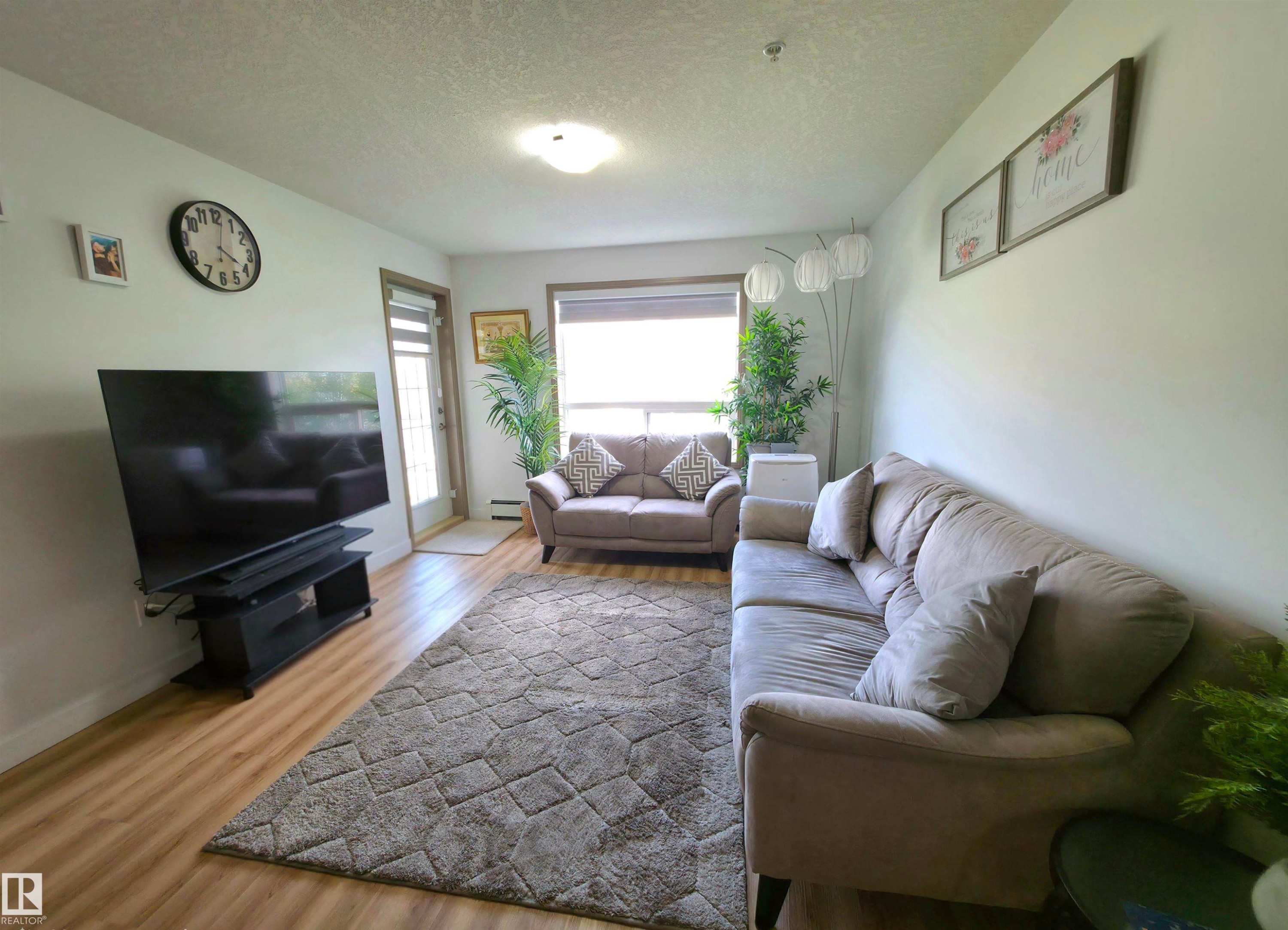 Living area featuring wood-finish flooring, white wall paint, and a door with an upper window panel - 210 5005 165 Avenue, Edmonton, AB - Indoor Photo Showing Living Room
