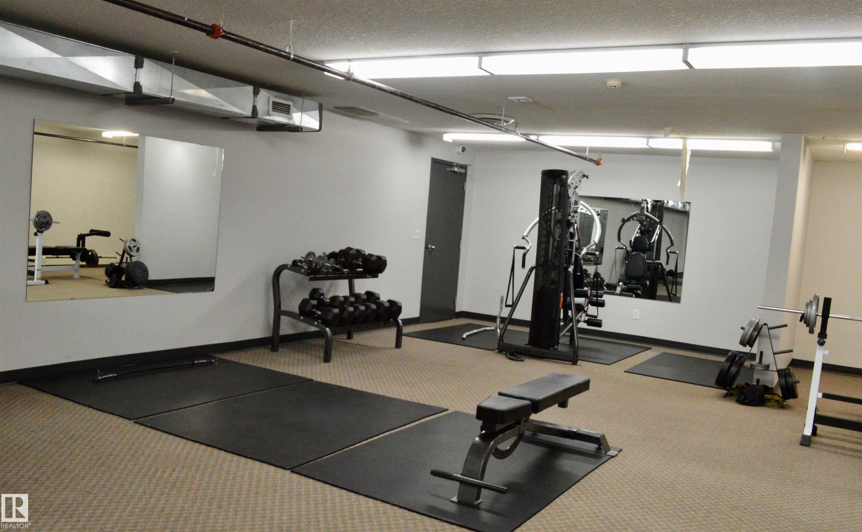 Dedicated fitness area featuring extensive floor space, wall-mounted mirrors, recessed lighting, exposed ductwork, and neutral carpeting with rubberized floor mats - 210 5005 165 Avenue, Edmonton, AB - Indoor Photo Showing Gym Room