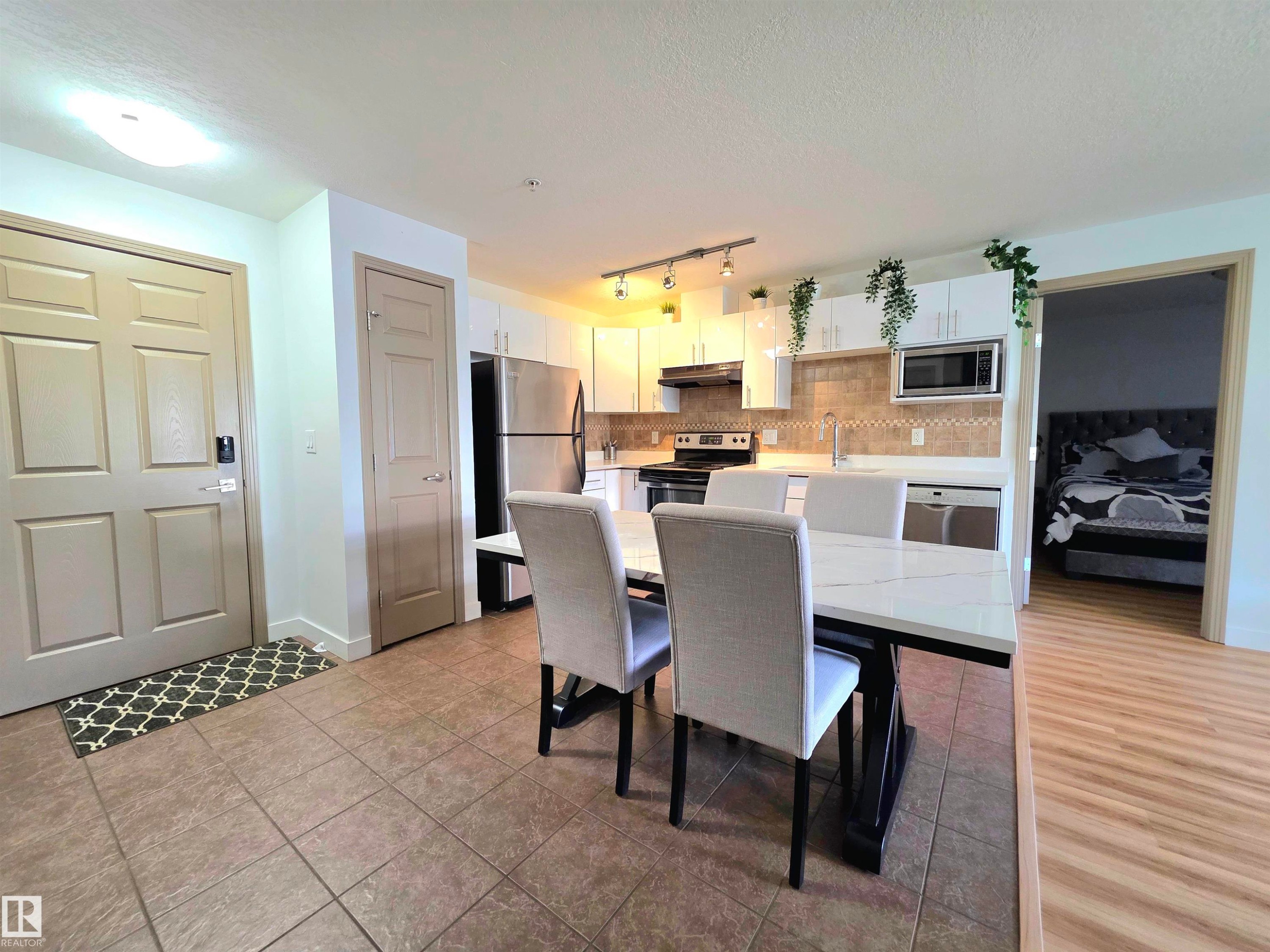 Open-concept kitchen and dining area featuring white cabinetry, stainless steel appliances, and a tiled backsplash - 210 5005 165 Avenue, Edmonton, AB - Indoor Photo Showing Other Room