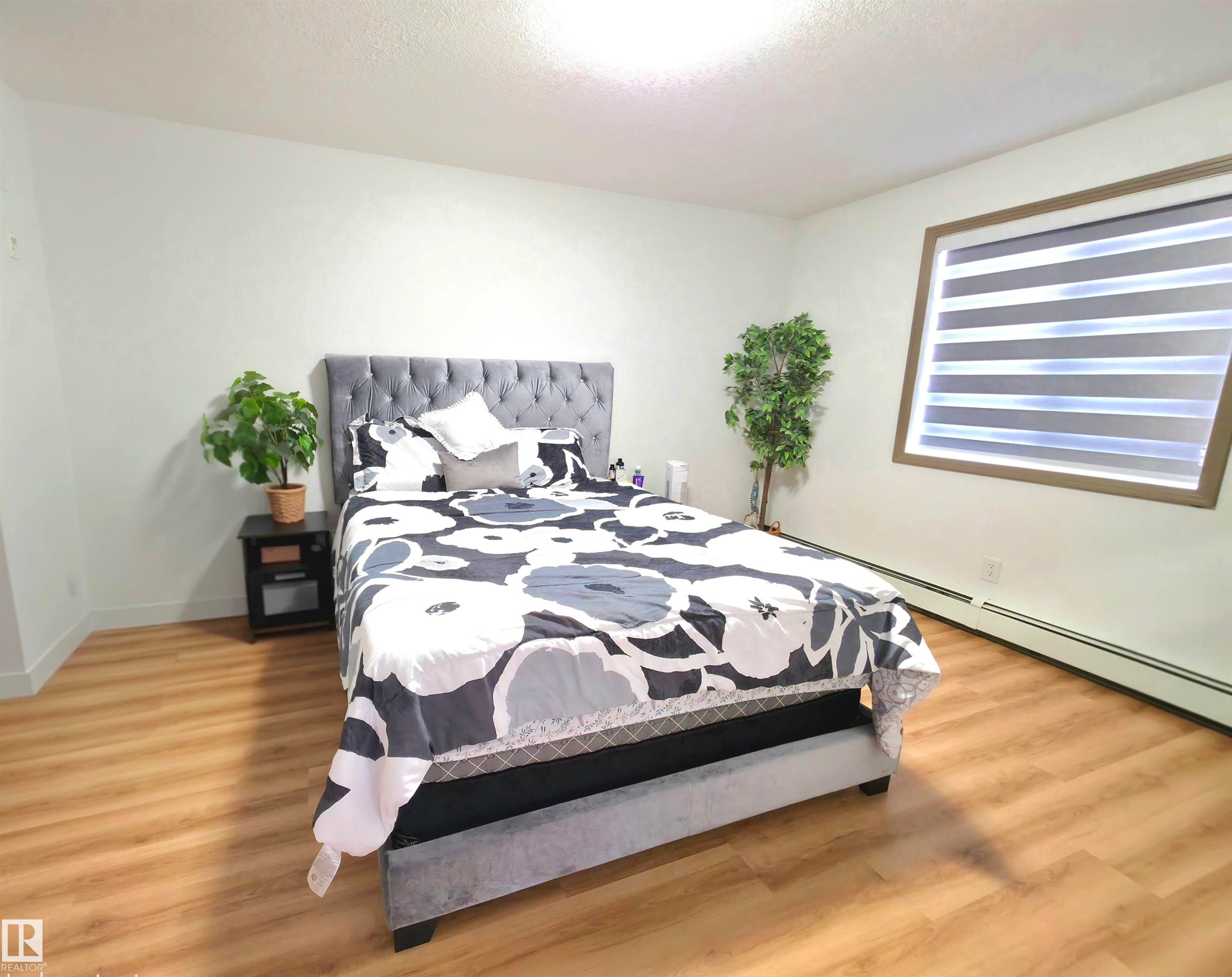 Bright room featuring wood-finish flooring, white walls, and a window with horizontal blinds and a brown frame - 210 5005 165 Avenue, Edmonton, AB - Indoor Photo Showing Bedroom