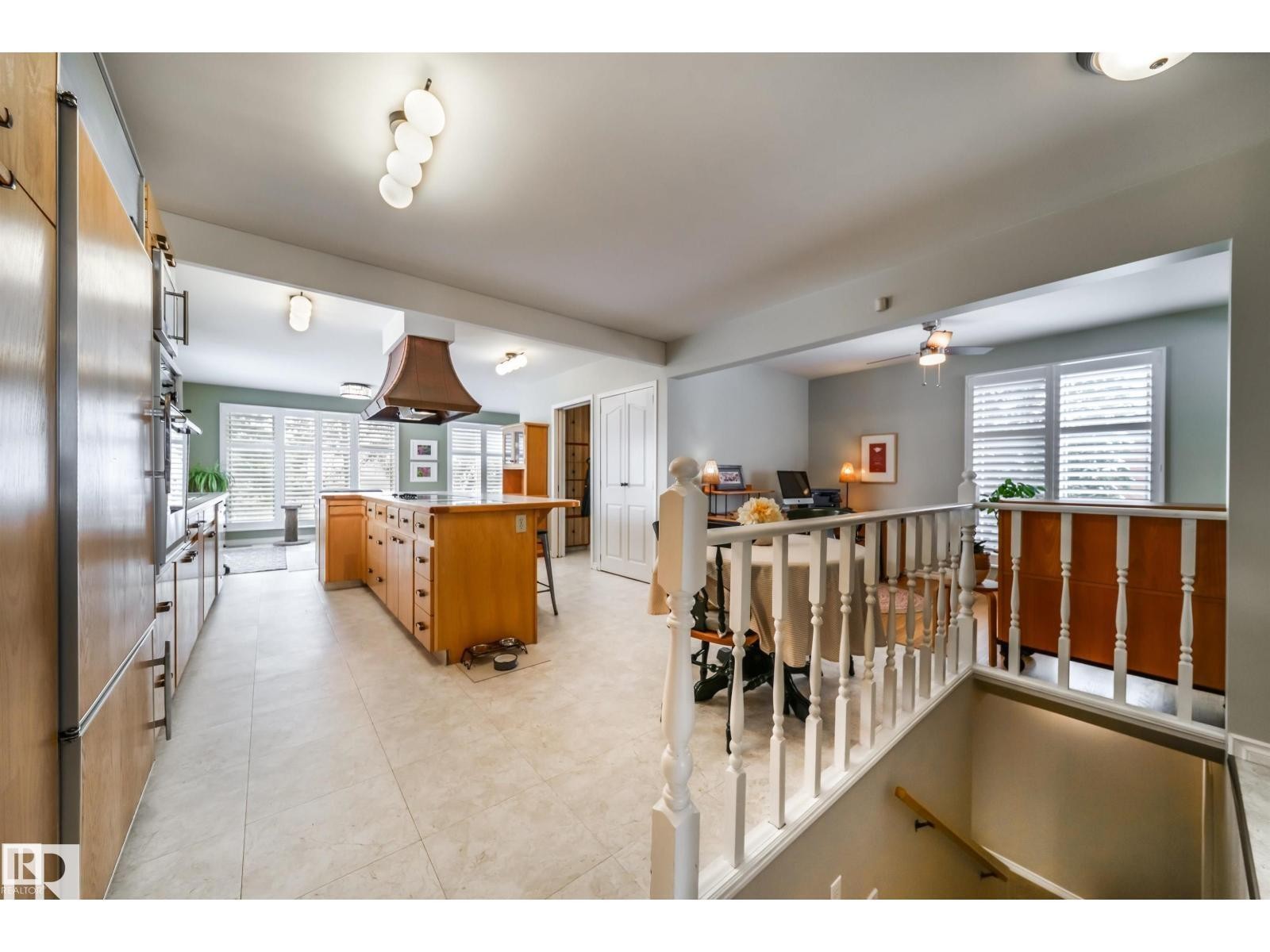 Spacious kitchen featuring a central island with integrated cooktop, warm wood-finish cabinetry, built-in double ovens, and tile flooring - 10231 46 Street, Edmonton, AB