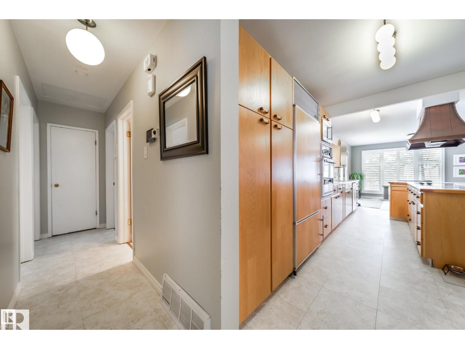 Expansive kitchen featuring light wood cabinetry, integrated refrigerator, double wall ovens, a large island with a cooktop, and a custom range hood - 10231 46 Street, Edmonton, AB