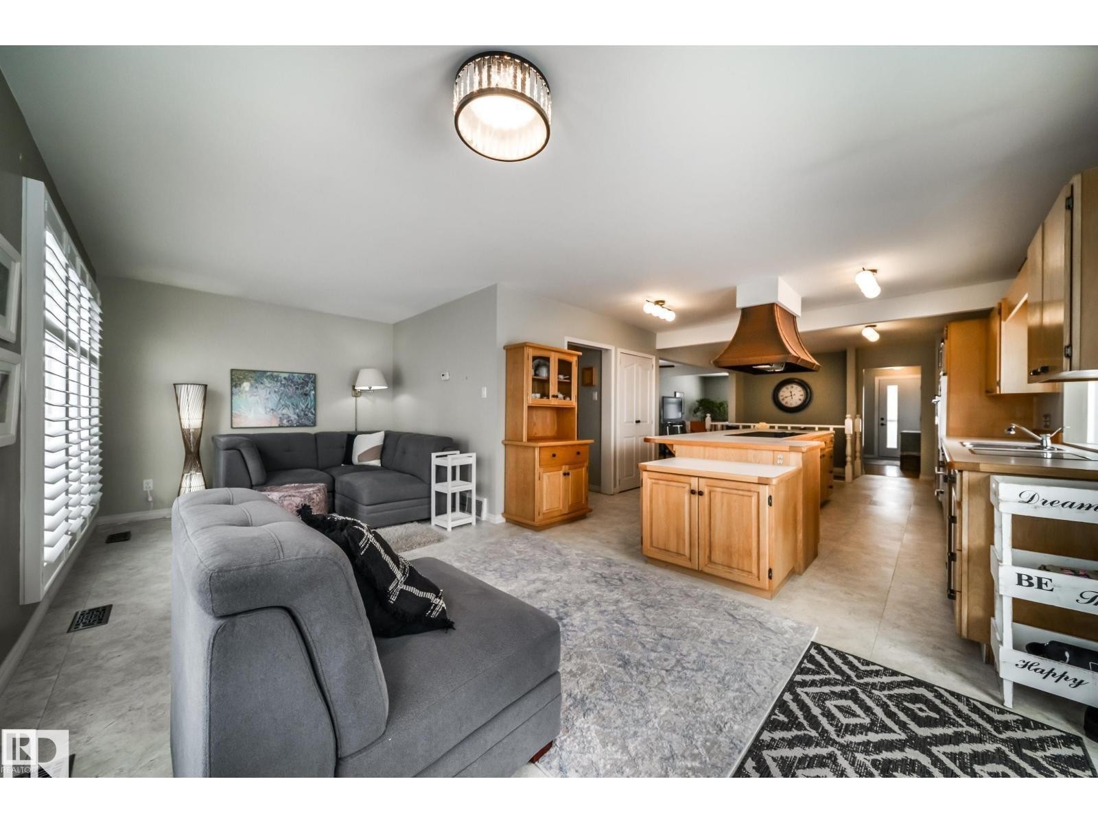 Open-concept living space with a kitchen island featuring wood-finish cabinetry, a copper-toned range hood, and light wood-finish countertops - 10231 46 Street, Edmonton, AB