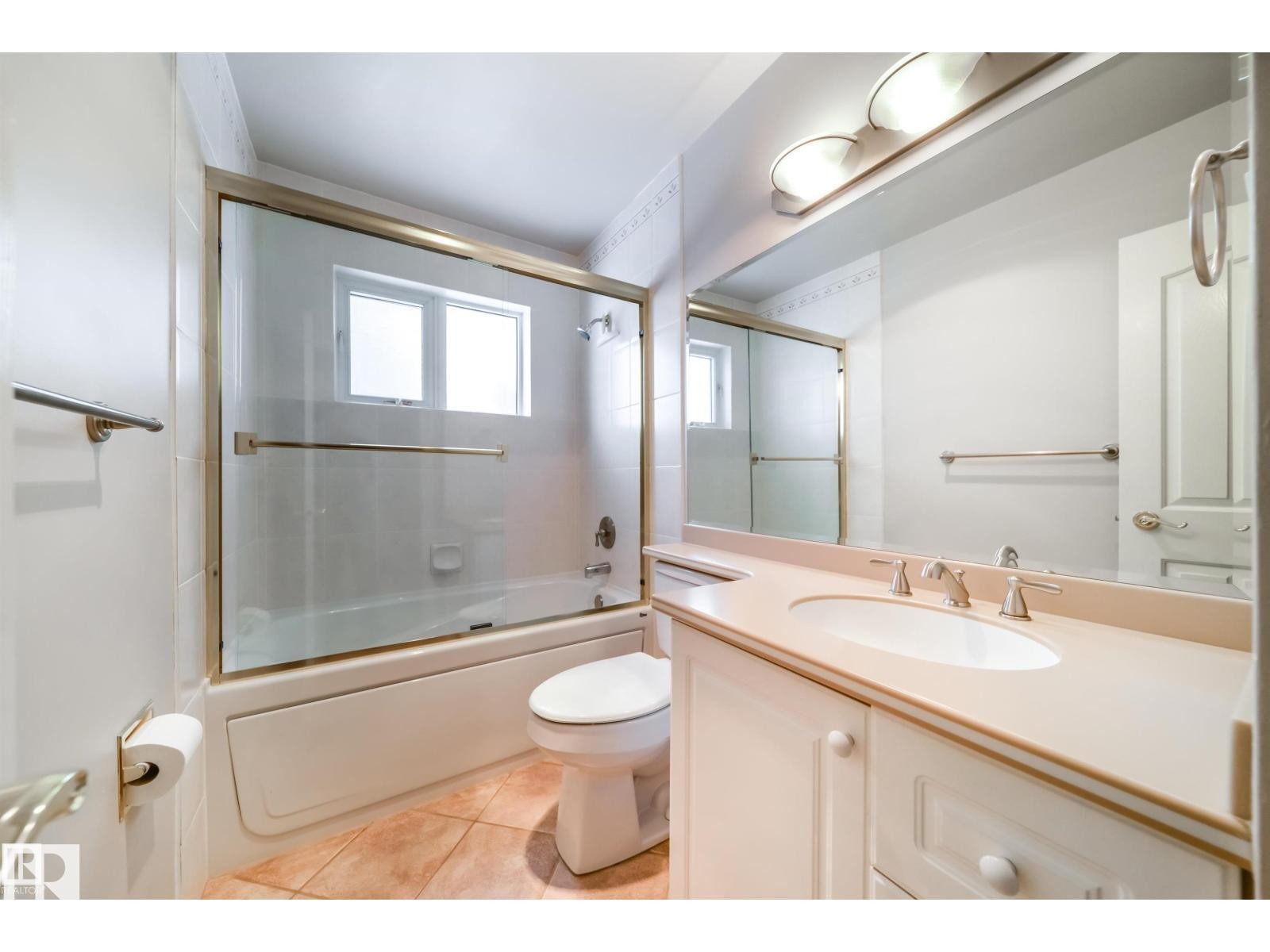 Bathroom featuring a vanity with an integrated sink and light-toned countertop, a large mirror, and a bathtub with a sliding glass enclosure - 10231 46 Street, Edmonton, AB
