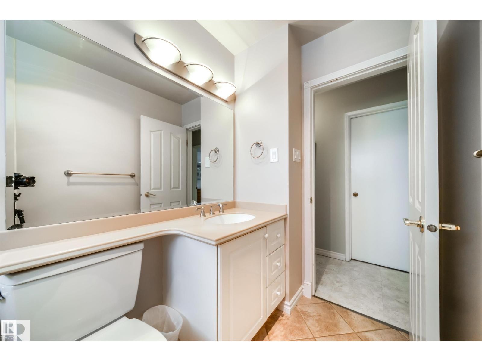 Bathroom featuring a single vanity with an integrated sink, three-light fixture, wall-mounted mirror, and tile flooring - 10231 46 Street, Edmonton, AB