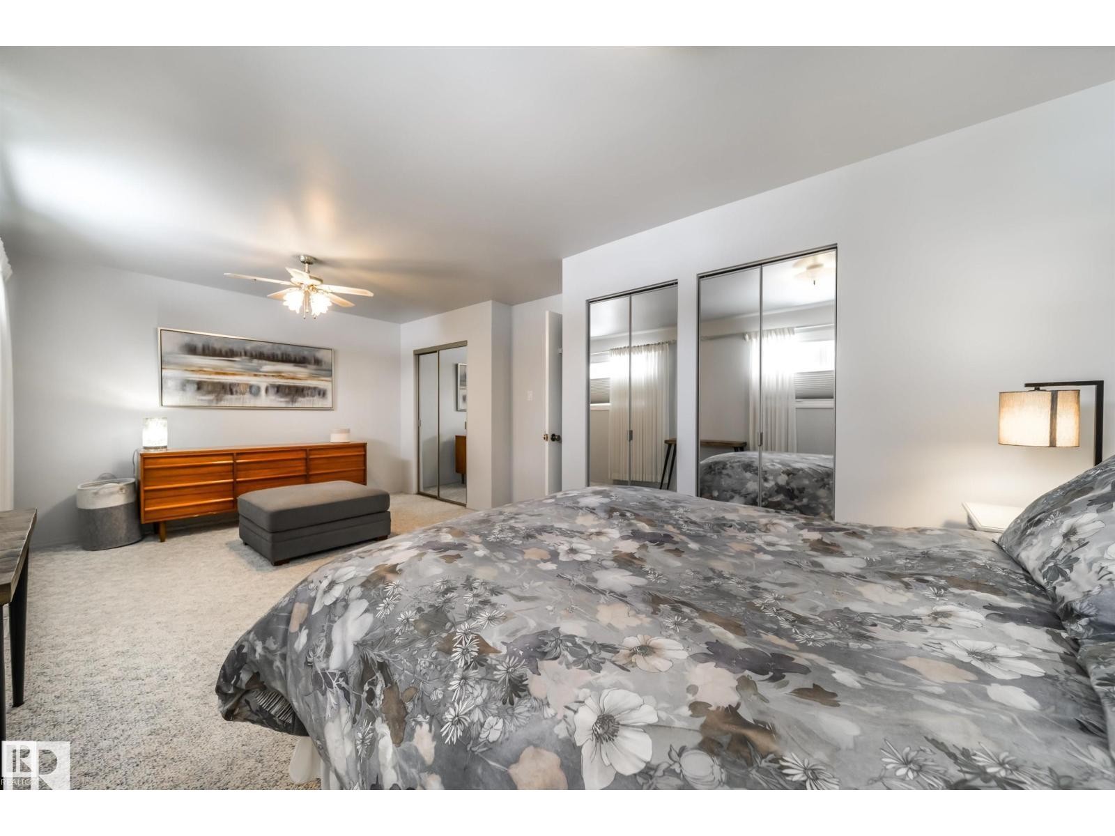 Carpeted bedroom featuring a ceiling fan, a wall of mirrored closet doors, a built-in closet with mirrored sliding doors, and a partial second built-in closet - 10231 46 Street, Edmonton, AB